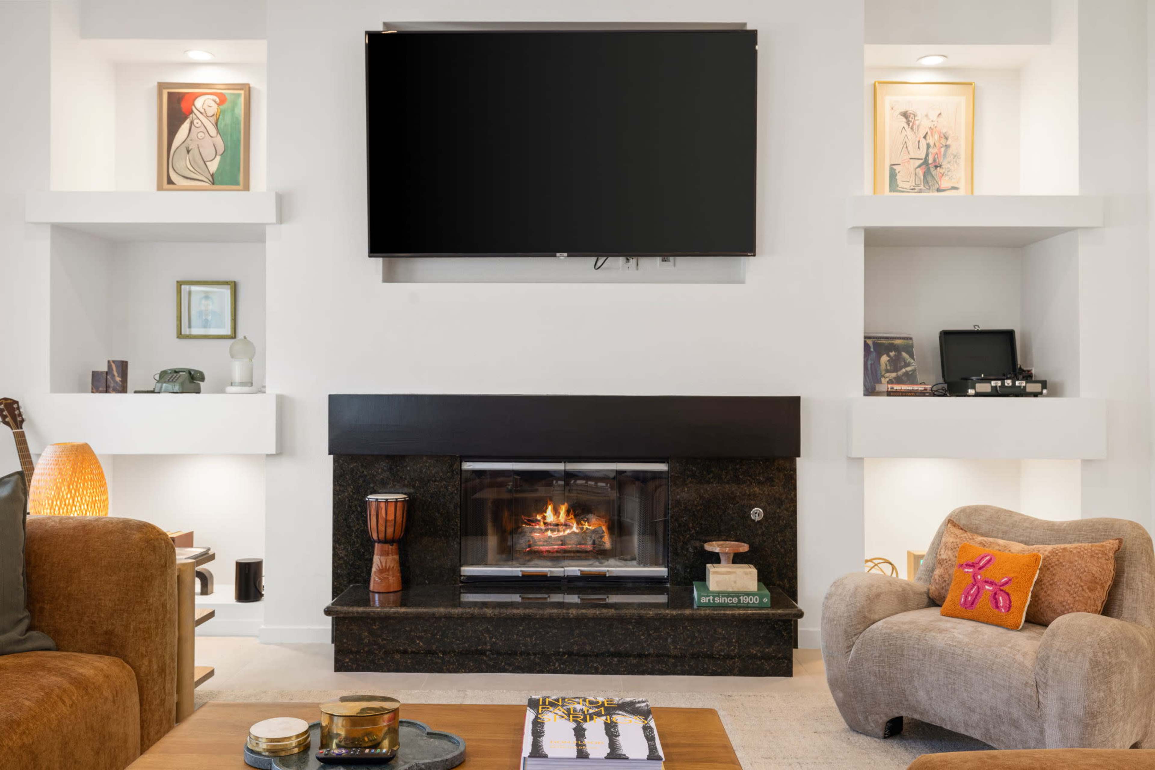 The living room features a central fireplace with a television mounted above it, flanked by two shelves displaying art and decorative items.