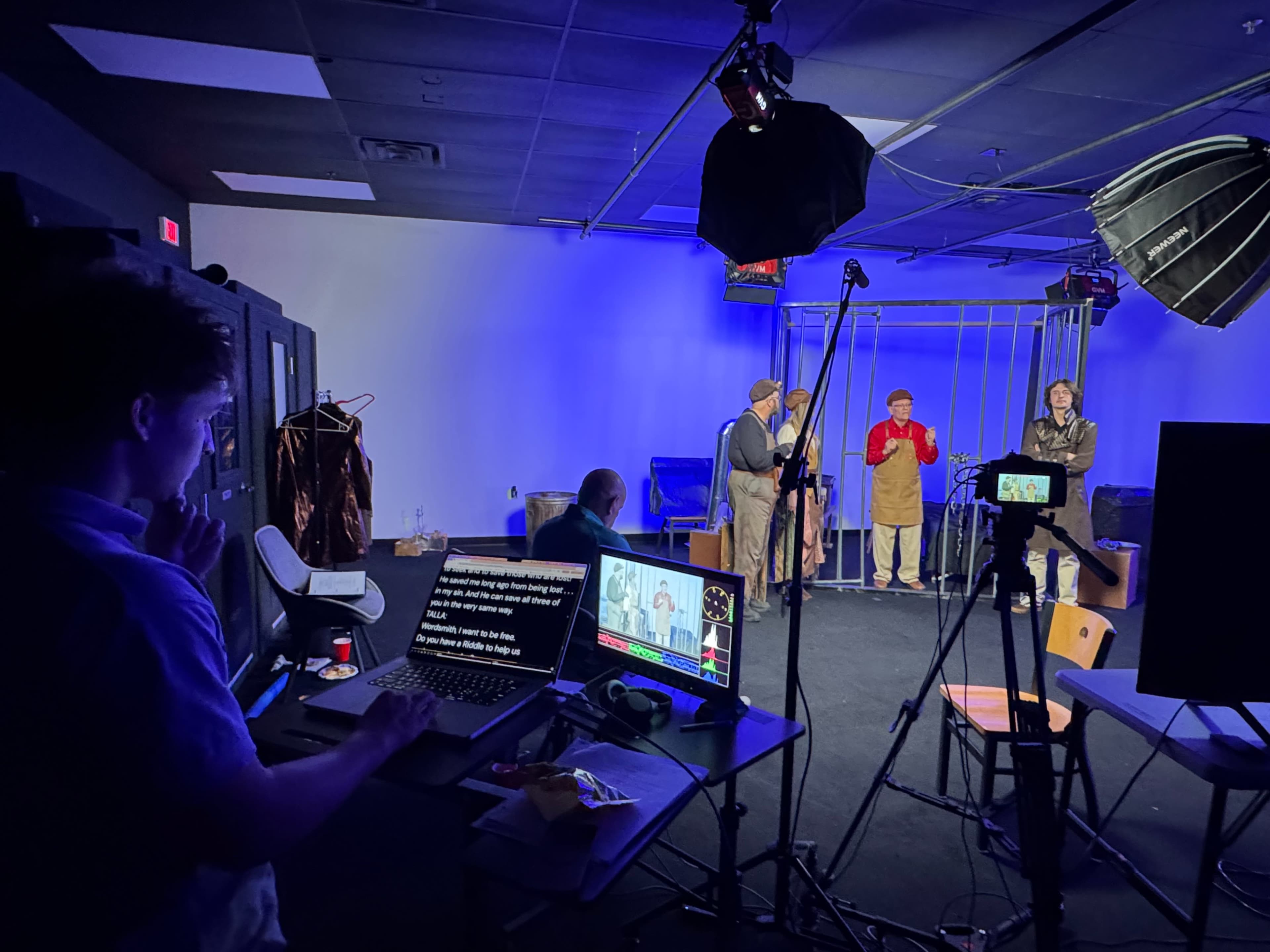 A studio setup features a crew preparing for a video shoot with actors in front of a backdrop and multiple cameras in use.