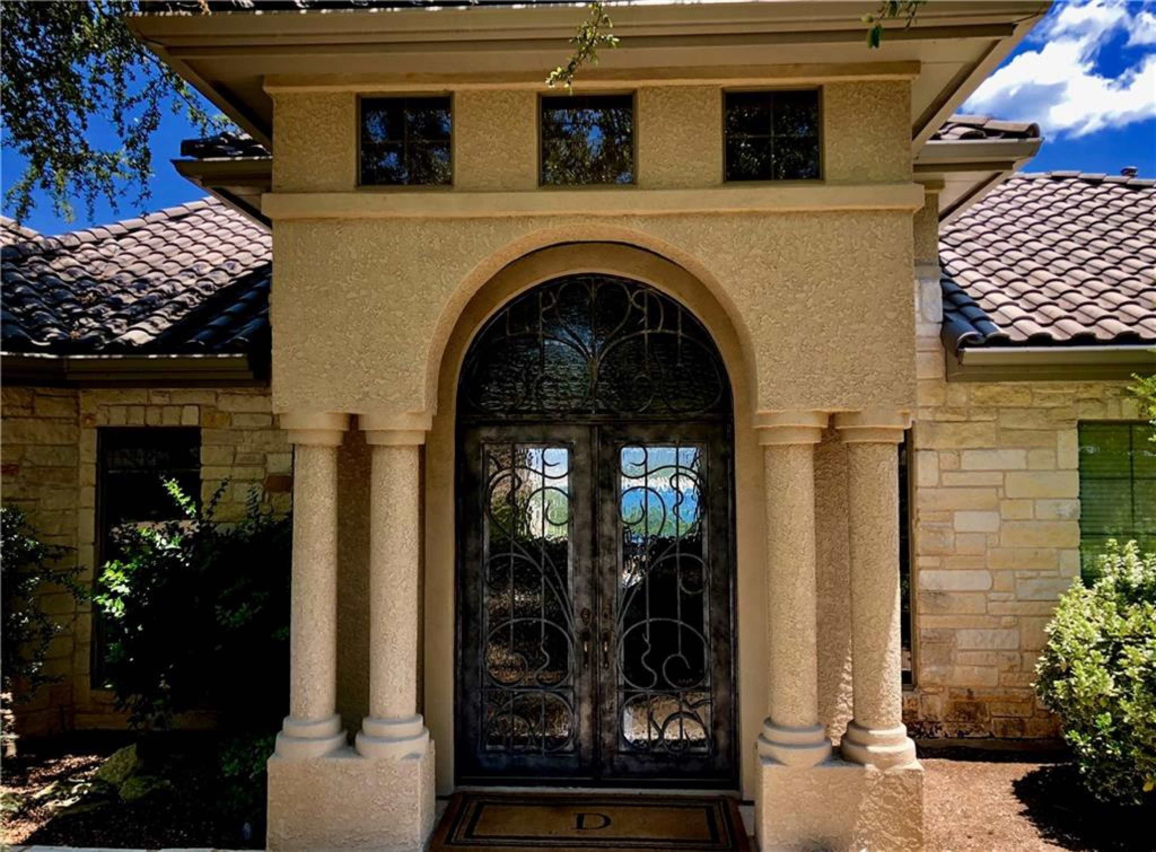 A house entrance featuring an arched doorway with a decorative metal door and stone columns.