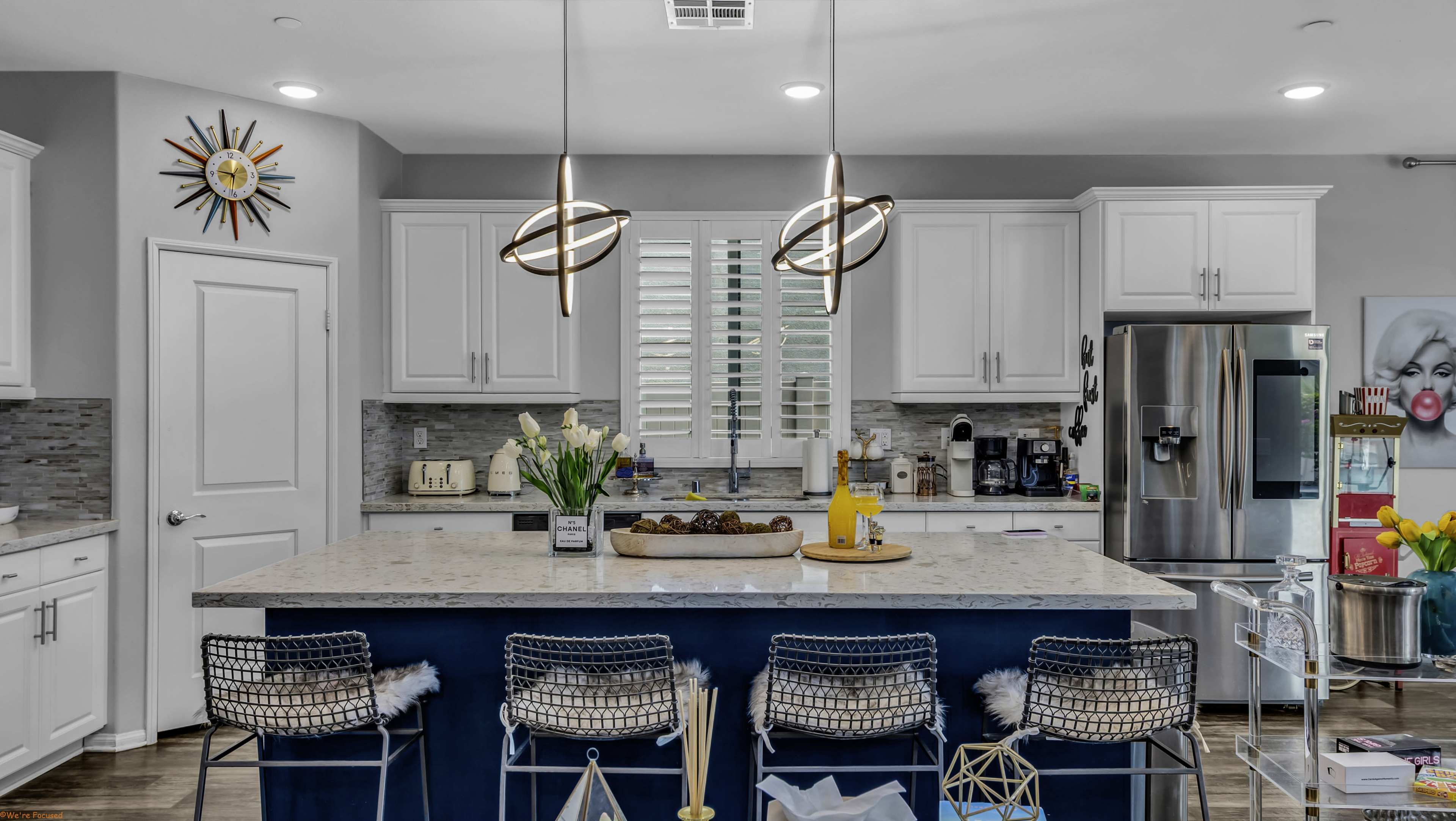 The kitchen features white cabinets, a large island with bar stools, and modern light fixtures, creating a spacious and bright cooking area.