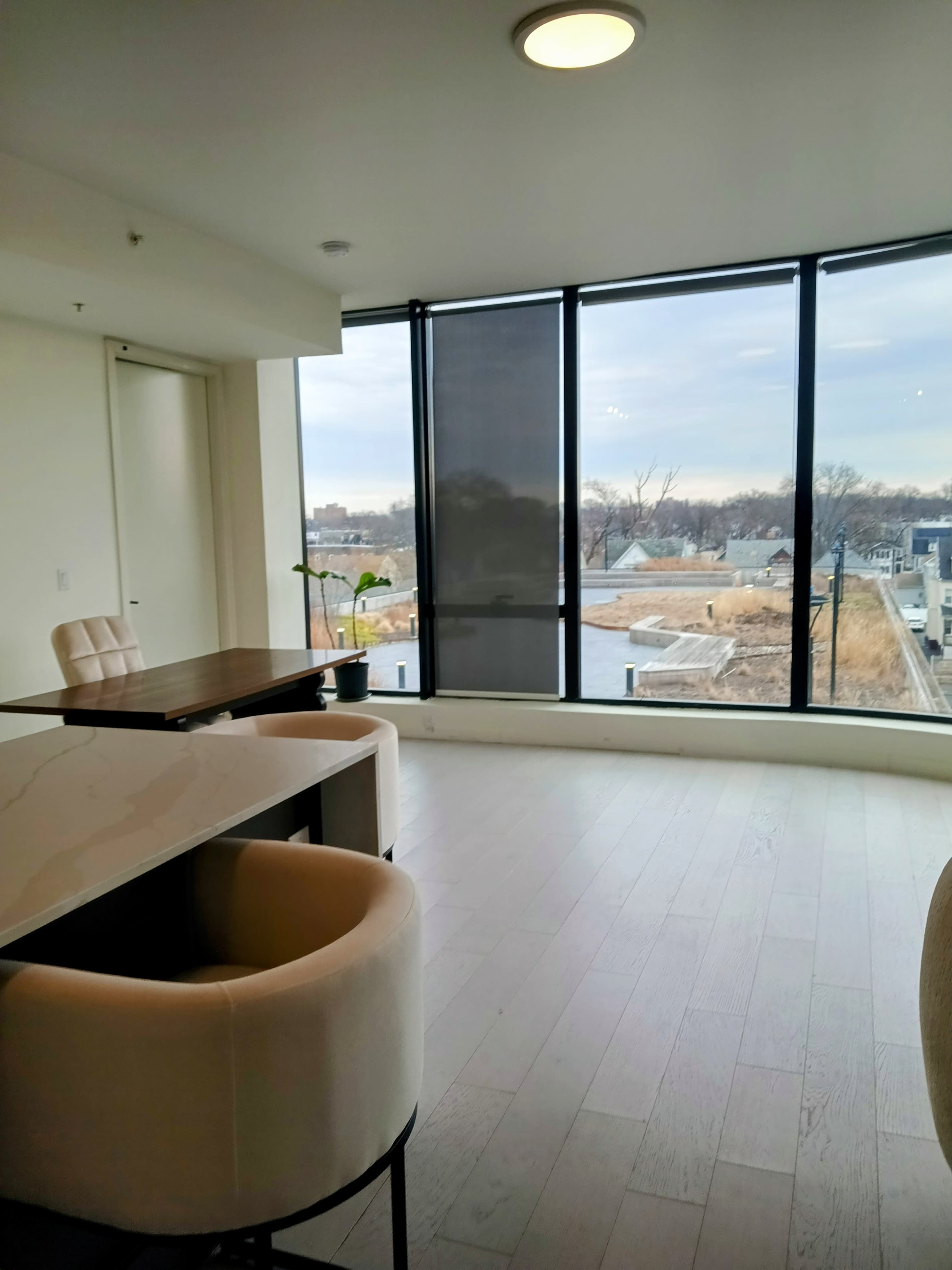 A modern interior features a table and two chairs beside large windows overlooking a landscaped area.