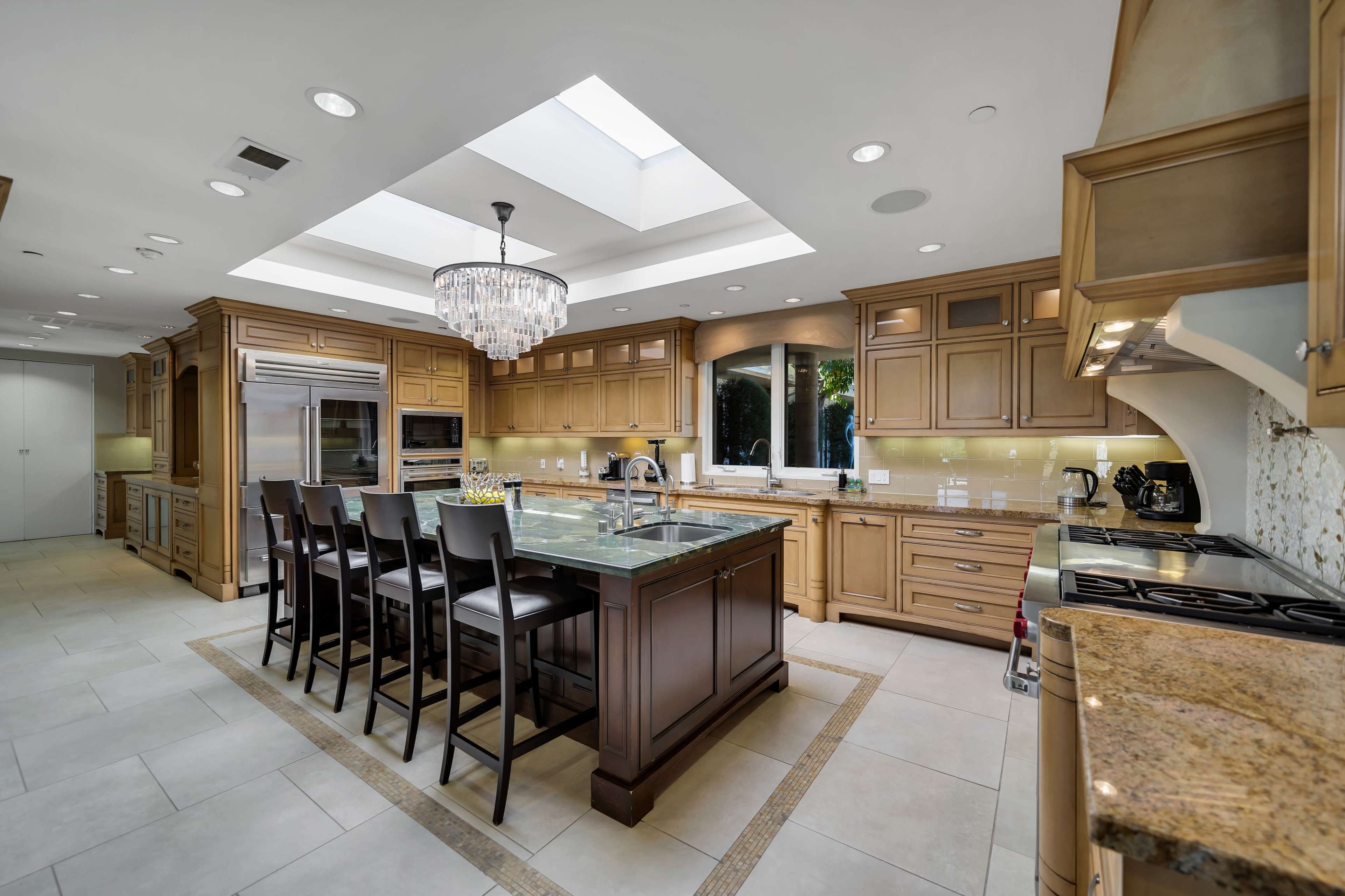A spacious kitchen features a central island with seating, wooden cabinetry, and a skylight that illuminates the area.