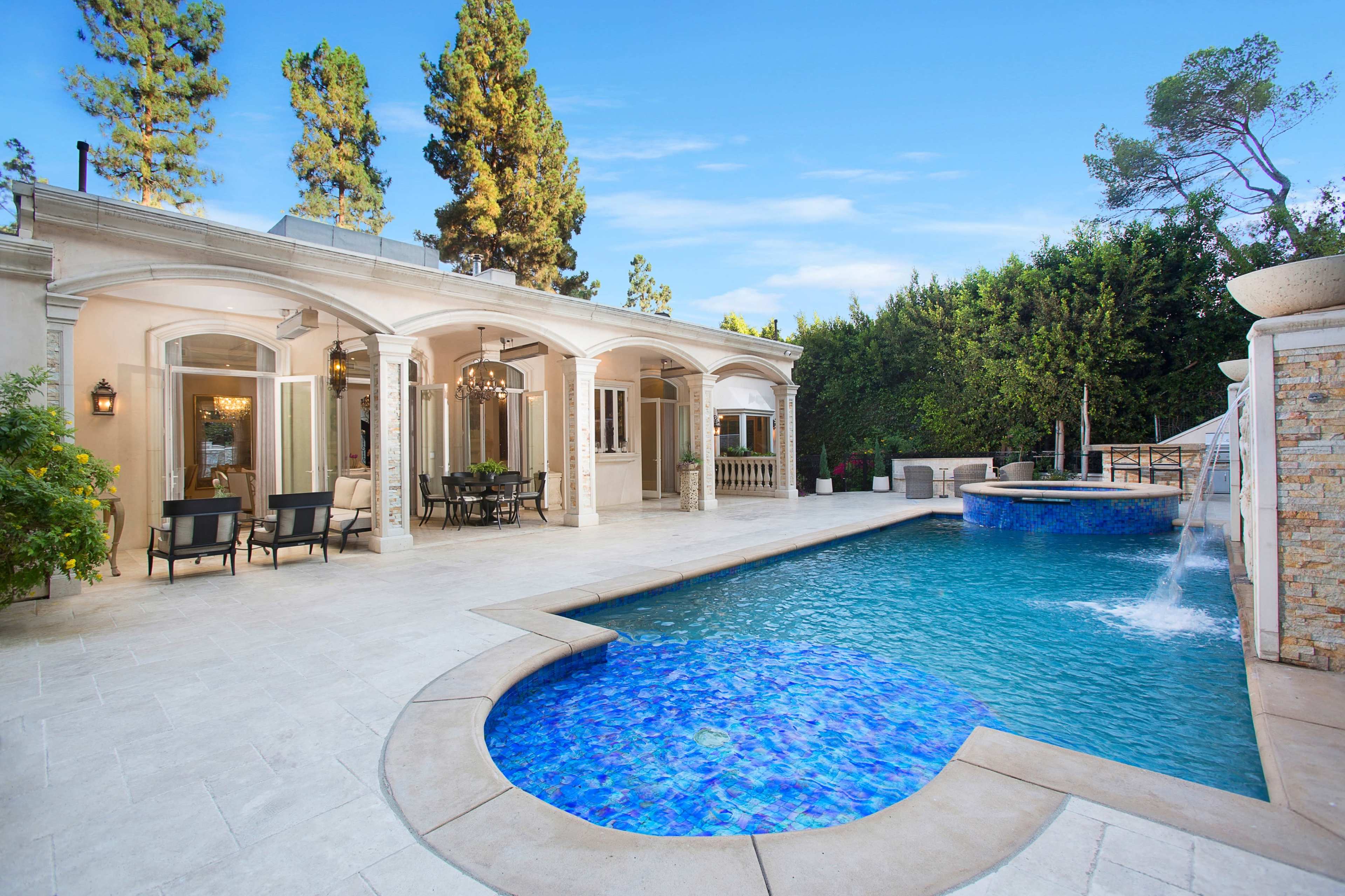A luxurious outdoor area featuring a swimming pool with a waterfall, surrounded by a stone-paved patio and elegant seating arrangements.