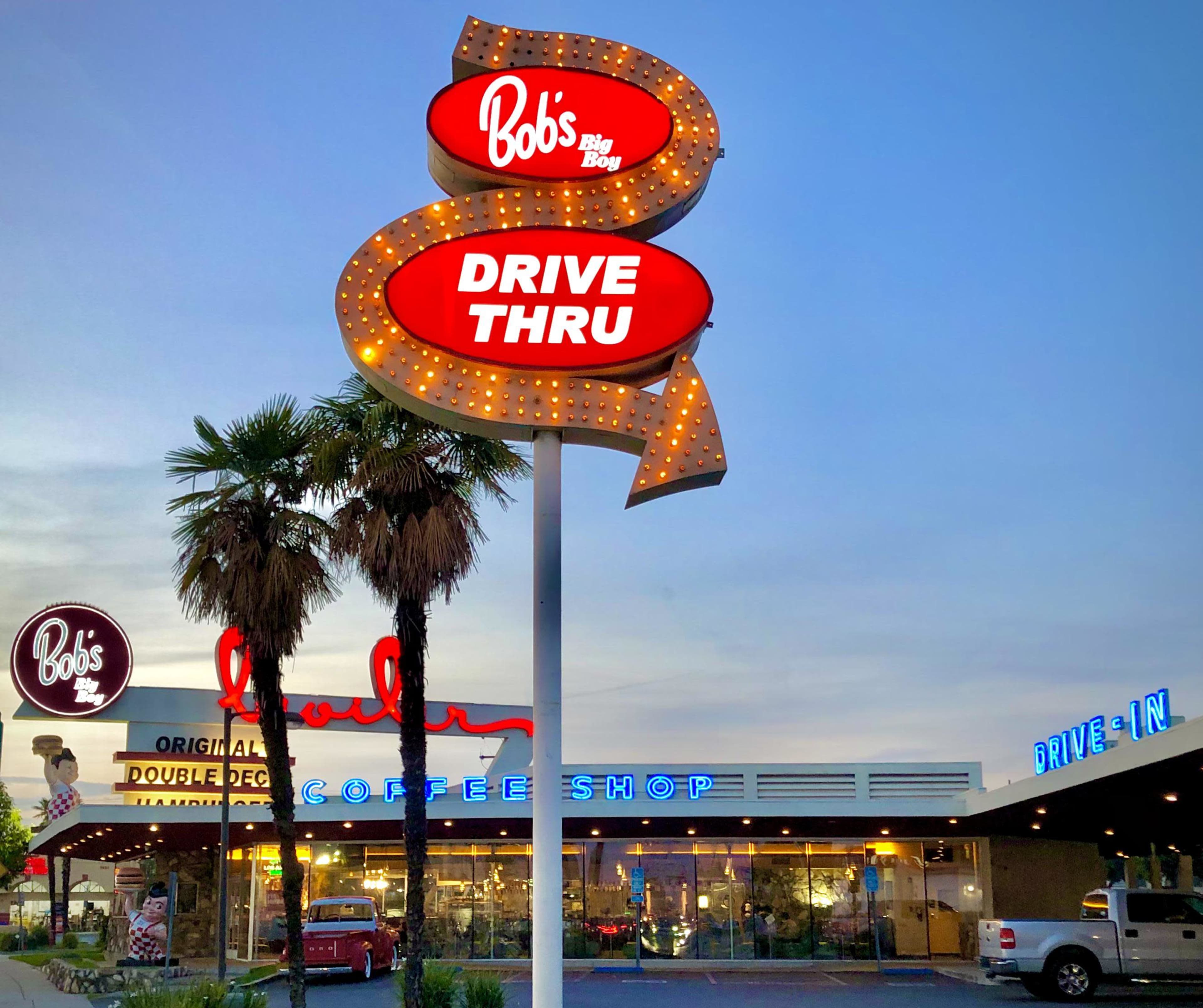 The image shows a retro-style diner sign for "Bob's Big Boy" with a drive-thru, set against the evening sky alongside the diner building featuring bright neon lights.