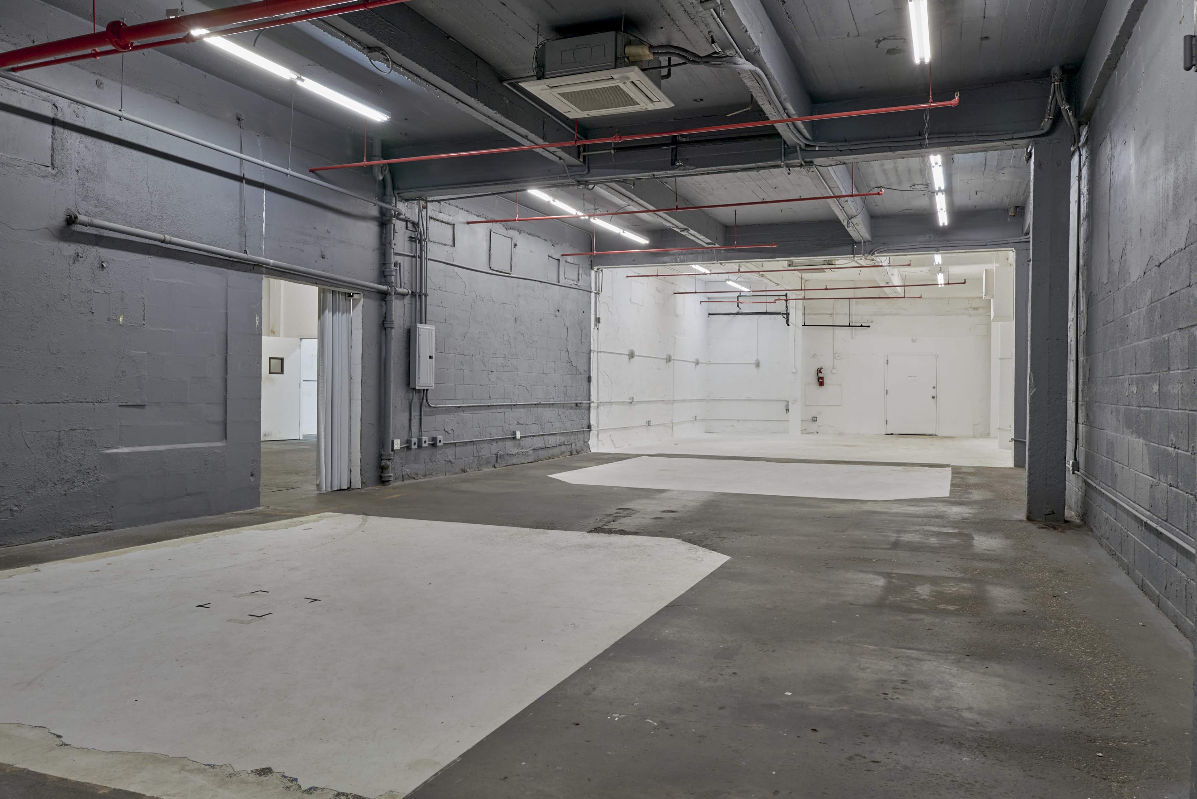 The image shows an empty industrial space with grey walls, overhead lighting, and a concrete floor.