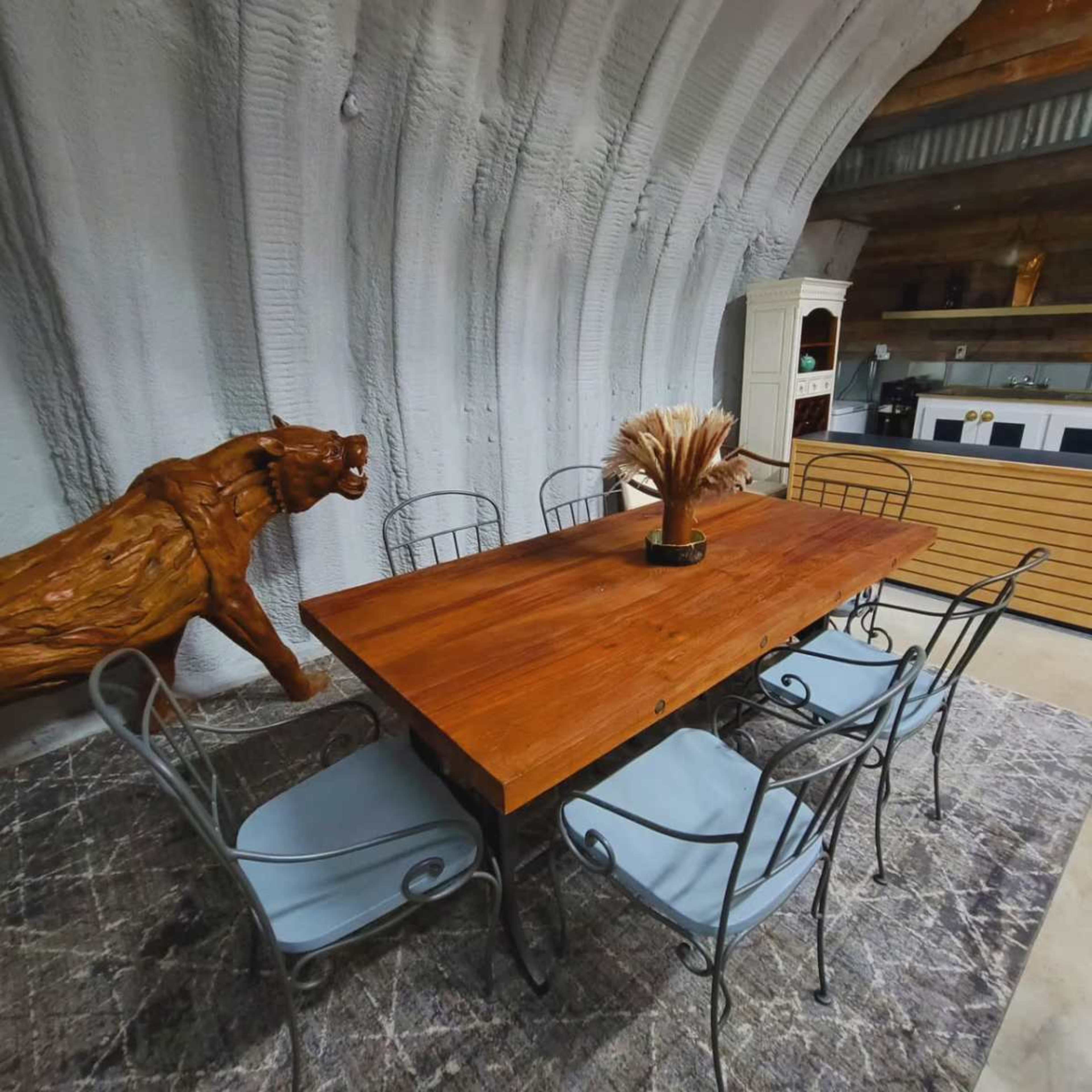A wooden table with six metal chairs is set in a room featuring a textured wall and a wooden sculpture of a lion nearby.