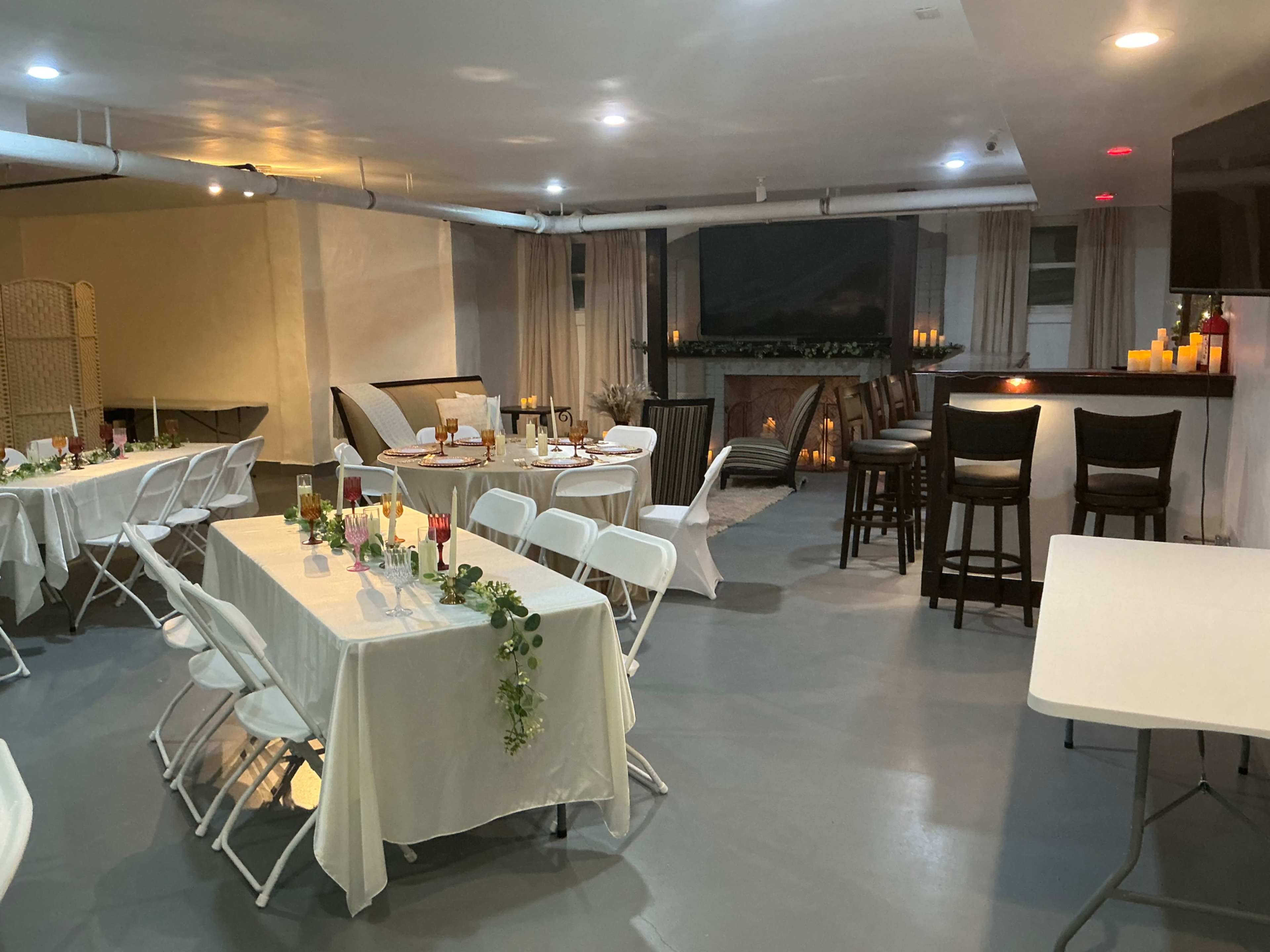 The image shows a spacious event room with tables set for dining, a bar area with high stools, and a large screen in the background.