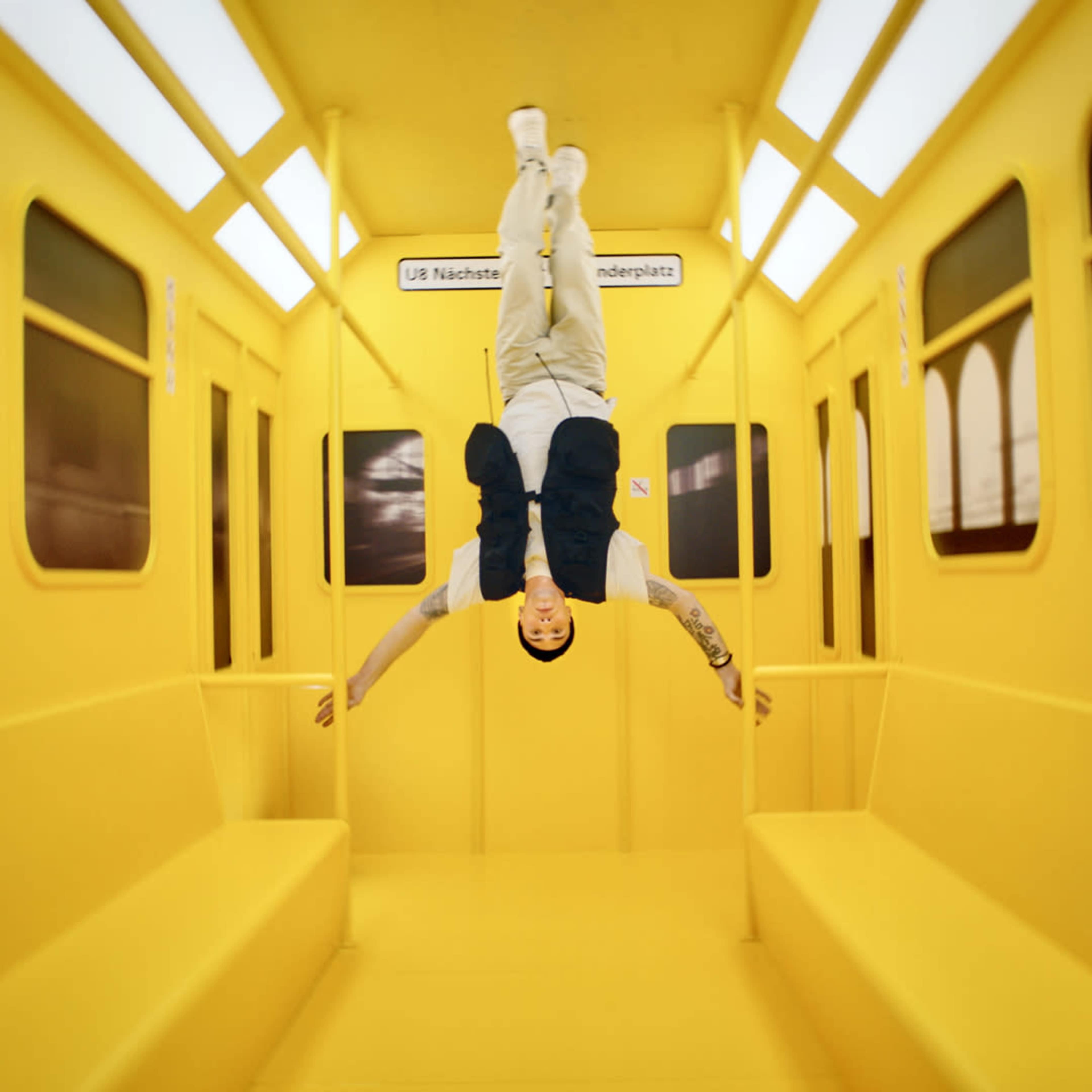 A person is hanging upside down inside a bright yellow subway train car.