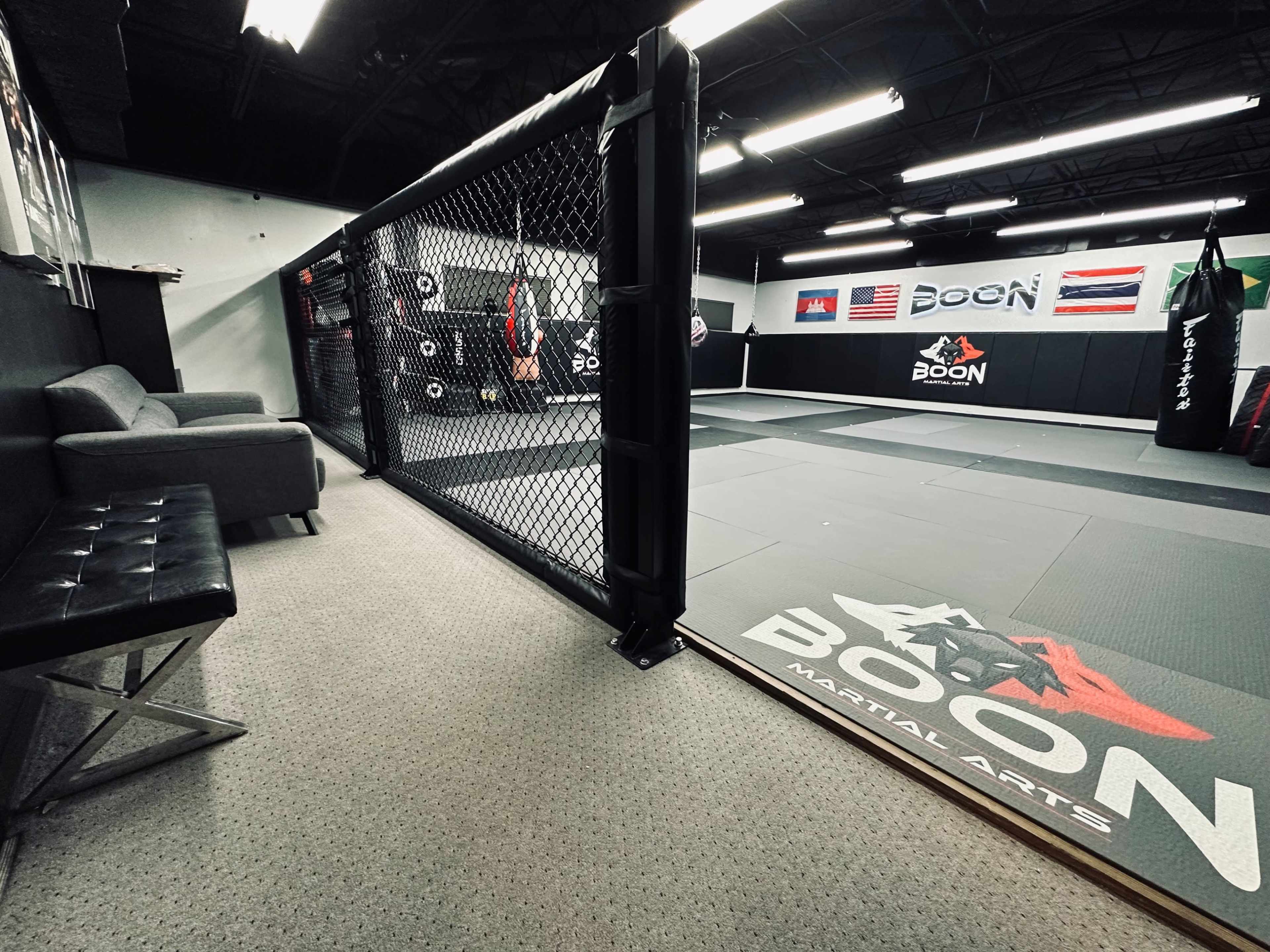 A martial arts training facility featuring a square mat area surrounded by a chain-link fence and various training equipment.