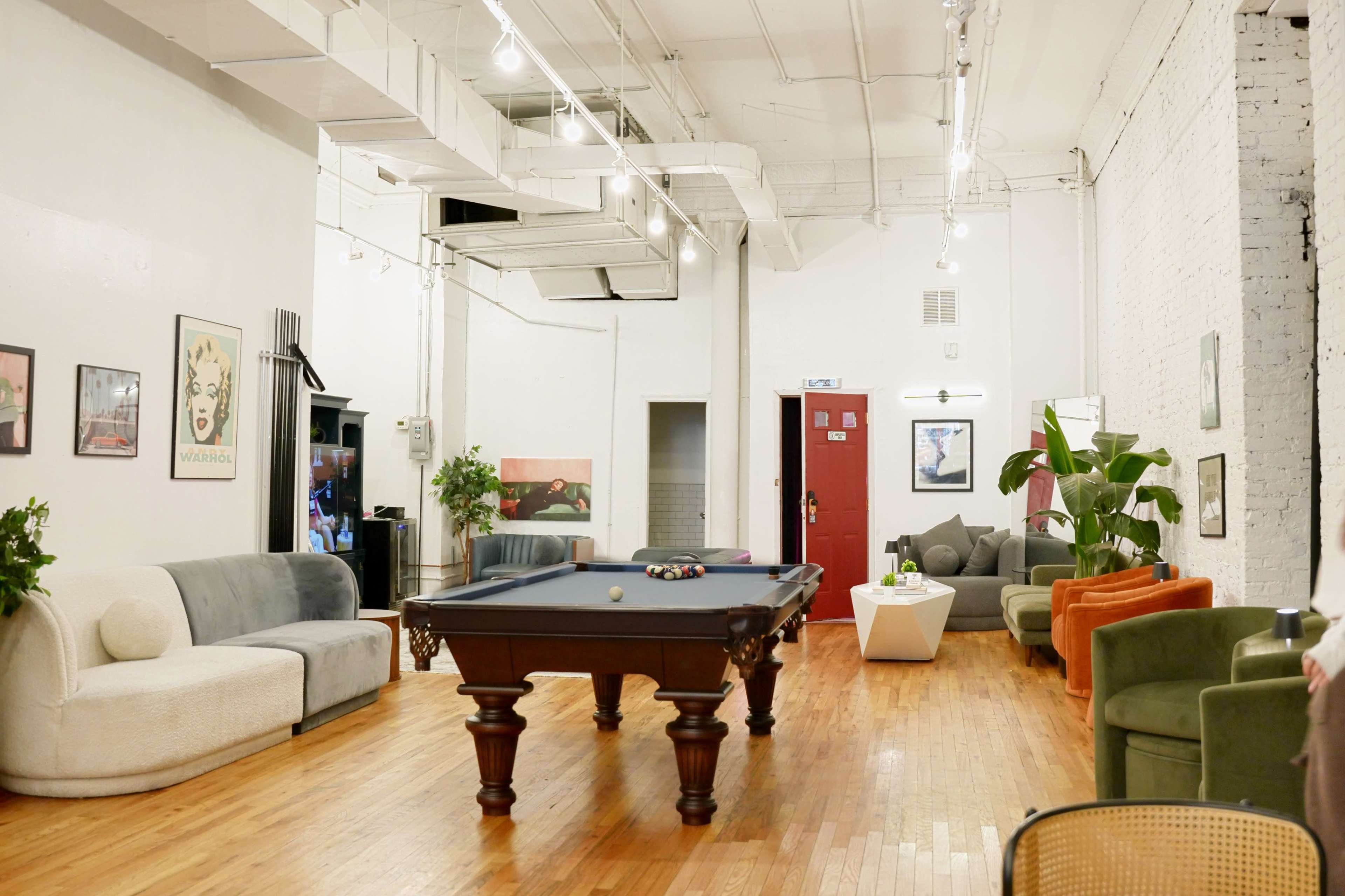 The image depicts a spacious lounge area featuring a billiard table in the center, surrounded by various seating options, including sofas and plants.