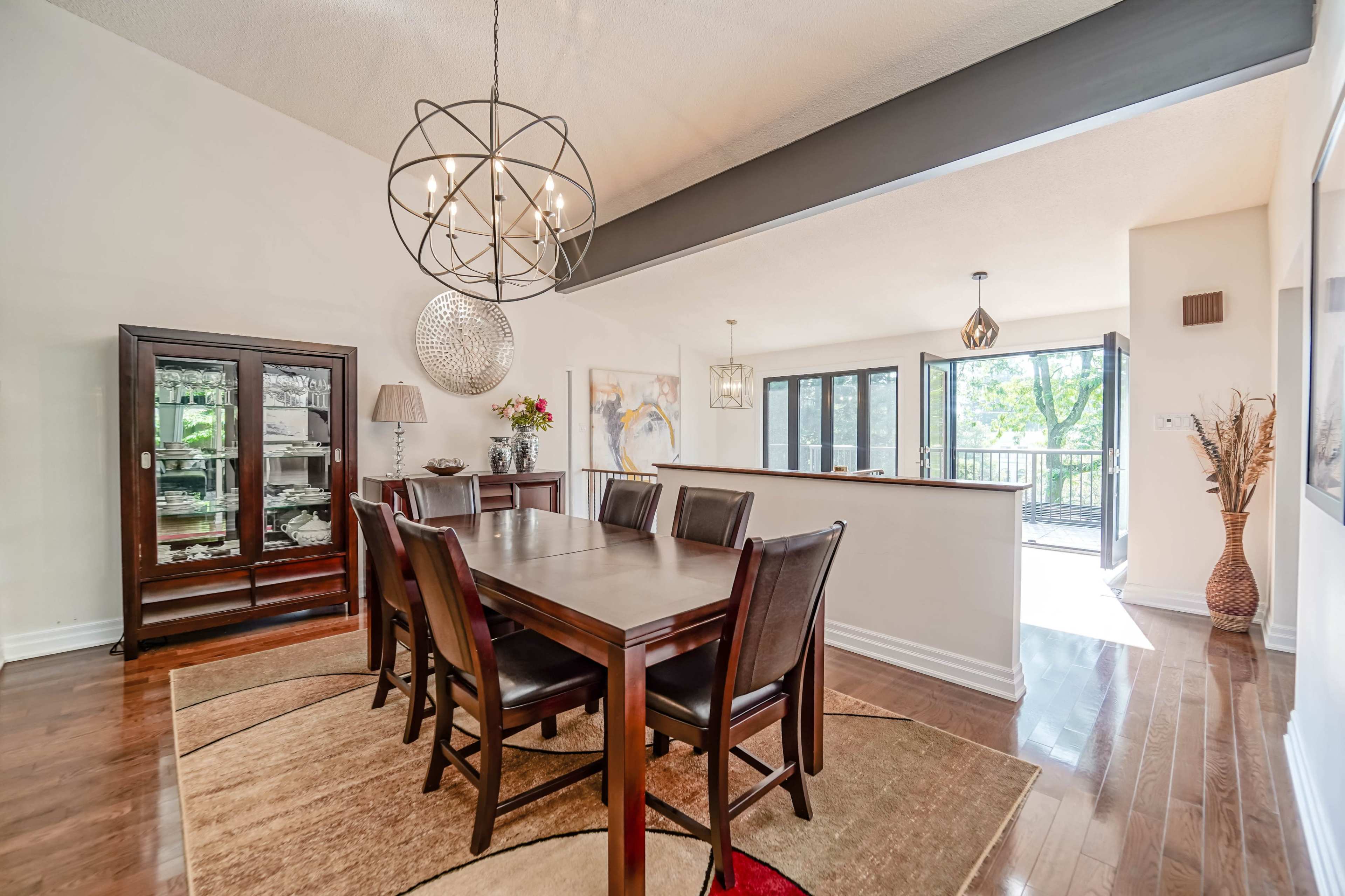 A spacious dining area features a large wooden table surrounded by chairs, with modern light fixtures and access to a balcony.