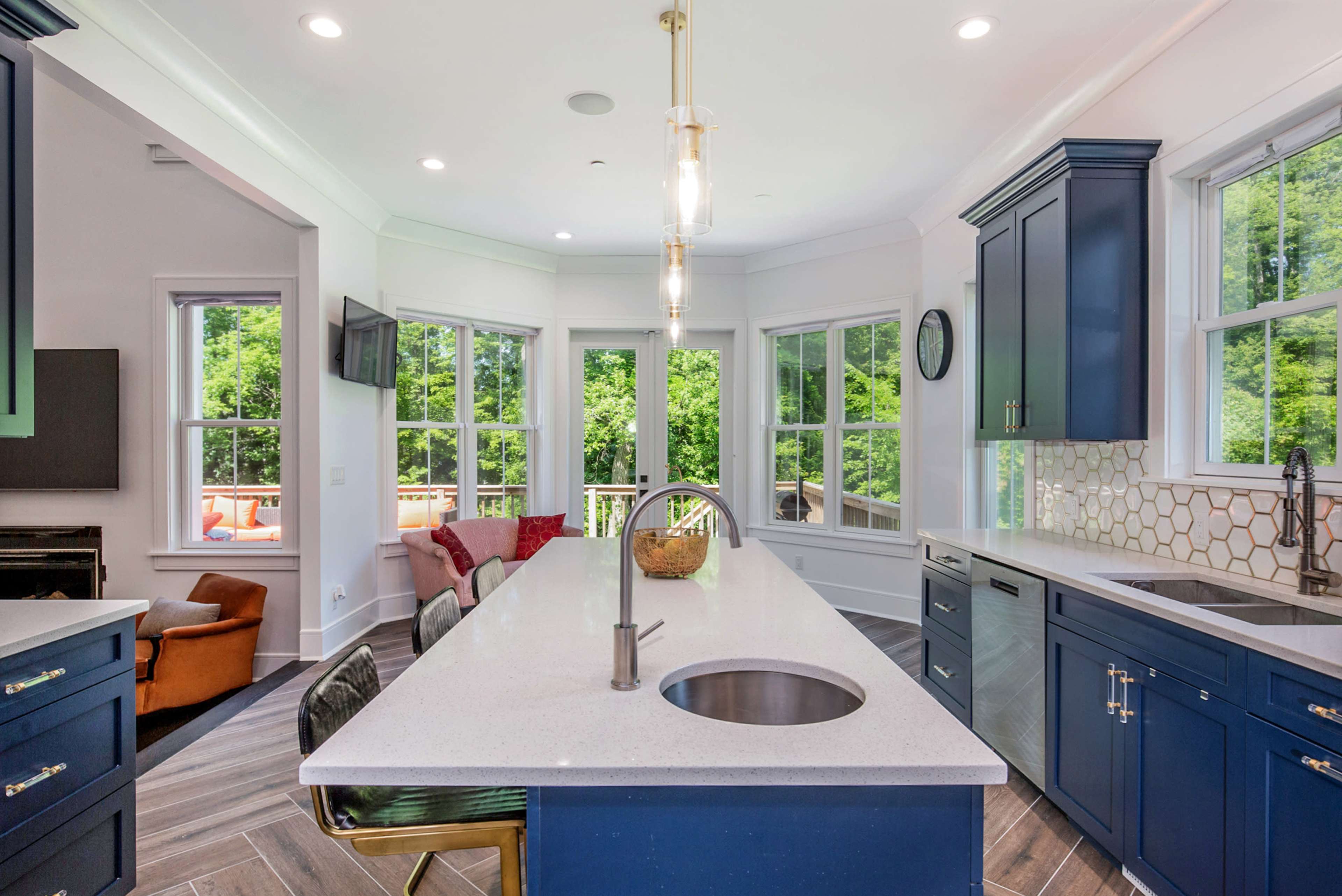 A modern kitchen with blue cabinetry, a large white countertop, and windows that overlook a green outdoor area.
