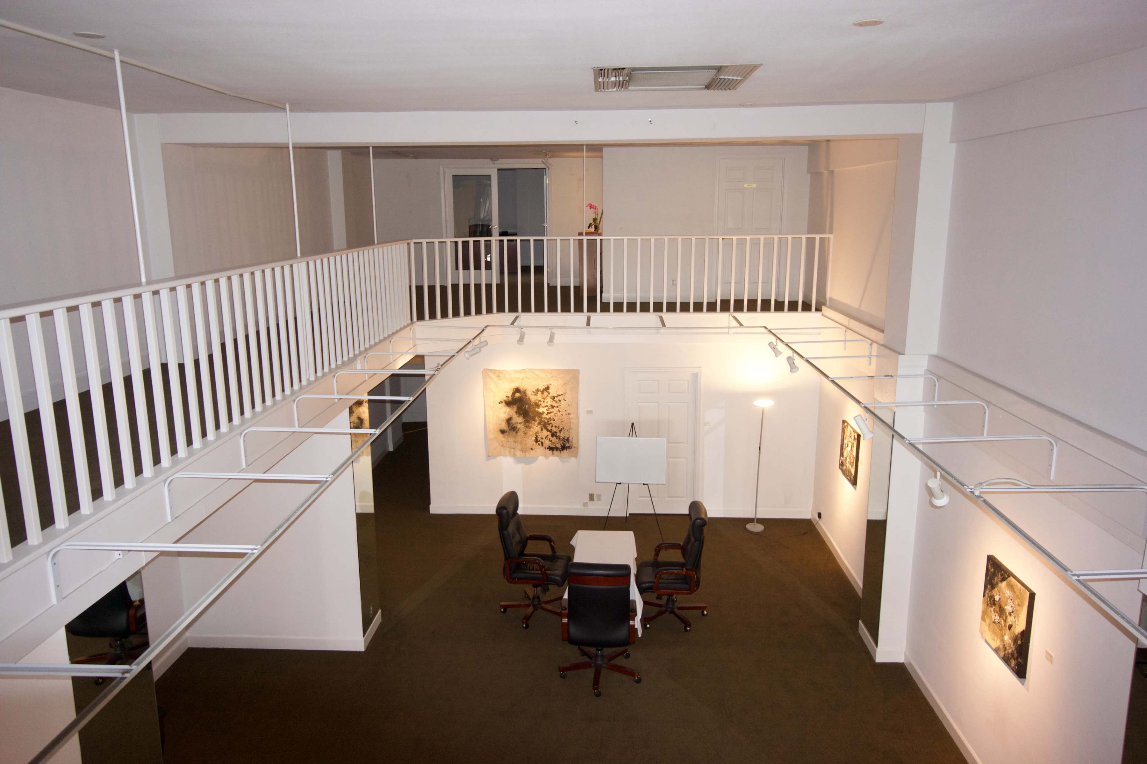 The image shows a spacious, modern office interior with a meeting area featuring a round table and four chairs, surrounded by white walls and artwork.