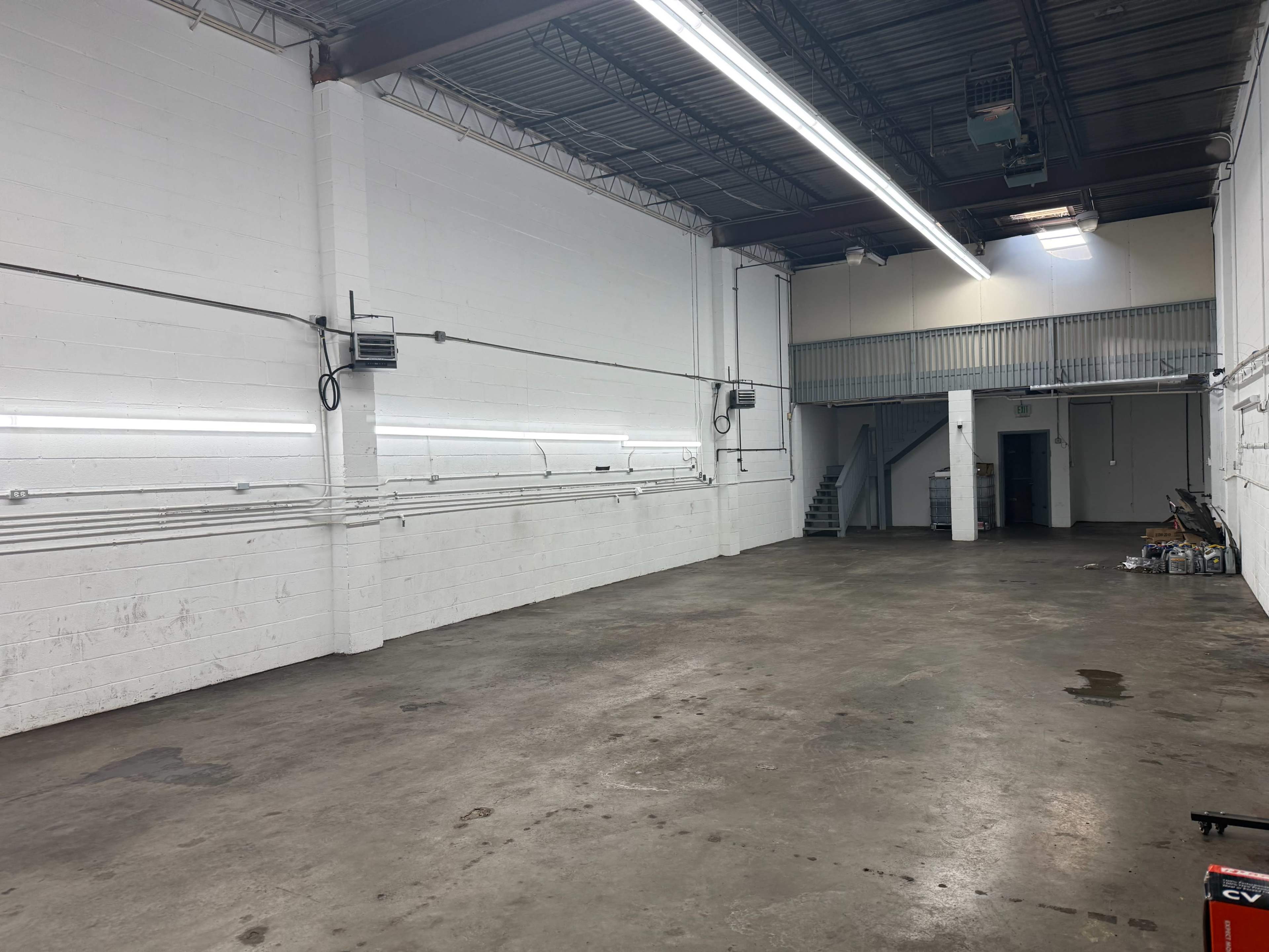 The image shows a large, empty warehouse space with white walls, concrete flooring, and some industrial lighting overhead.