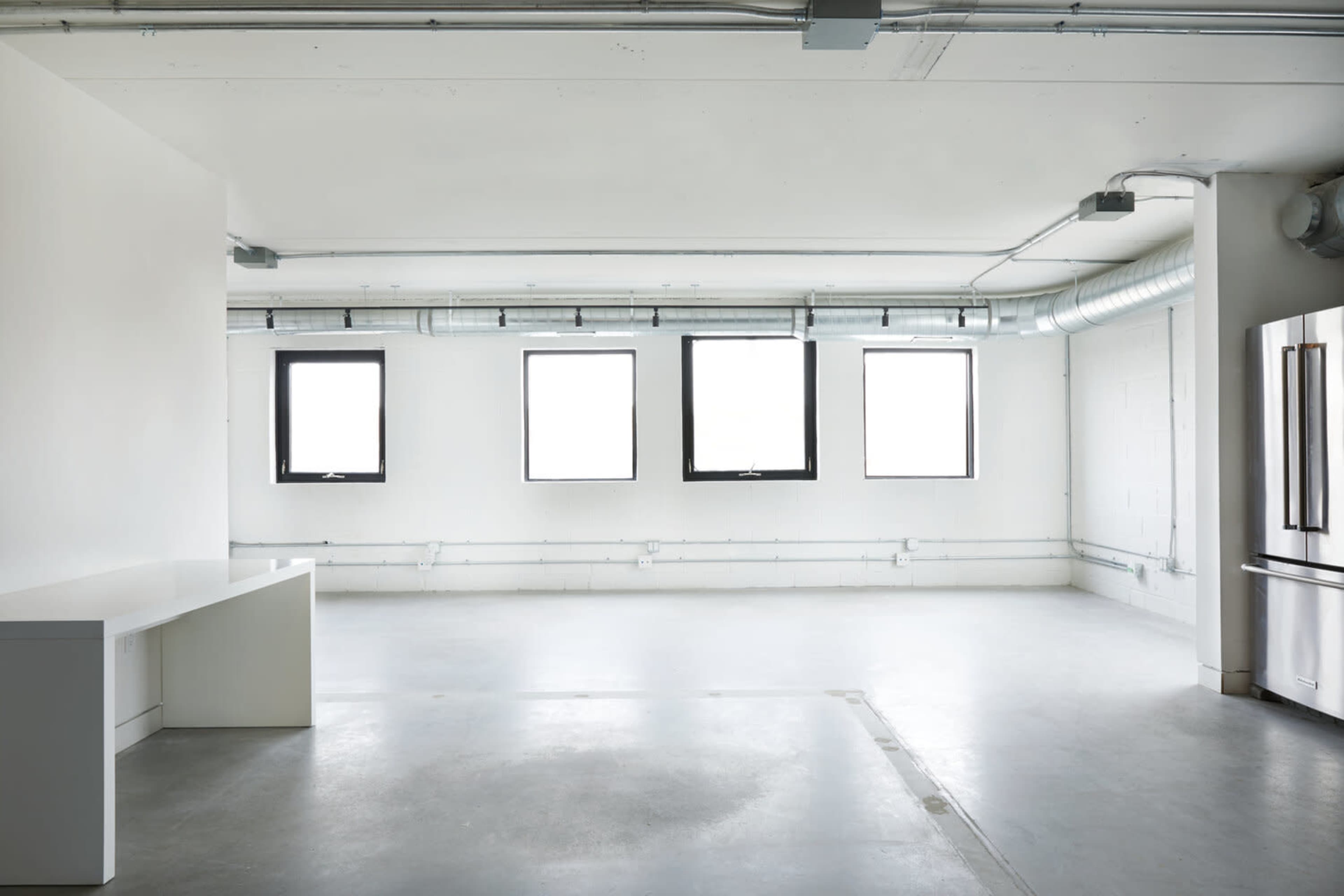 An empty room features a long, white counter and three large windows along one wall.