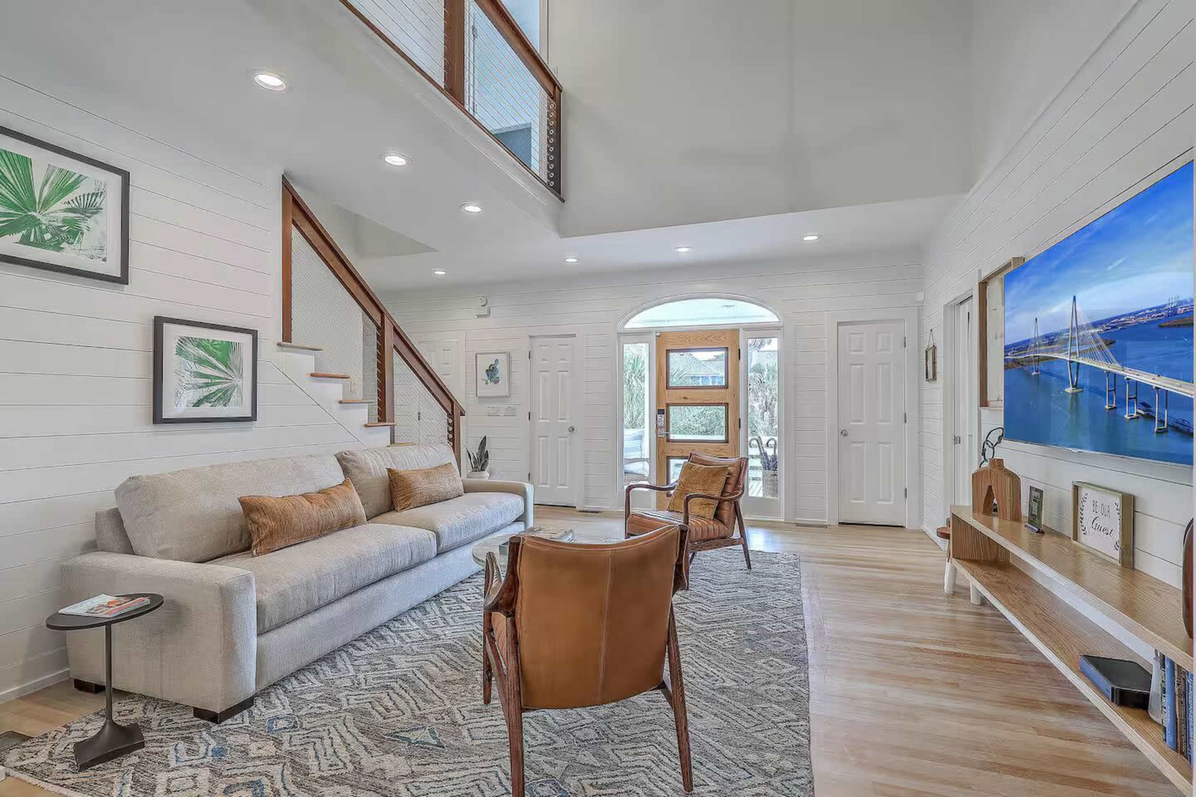 The living room features a light-colored sofa, two brown armchairs, and a large window that allows natural light to fill the space.