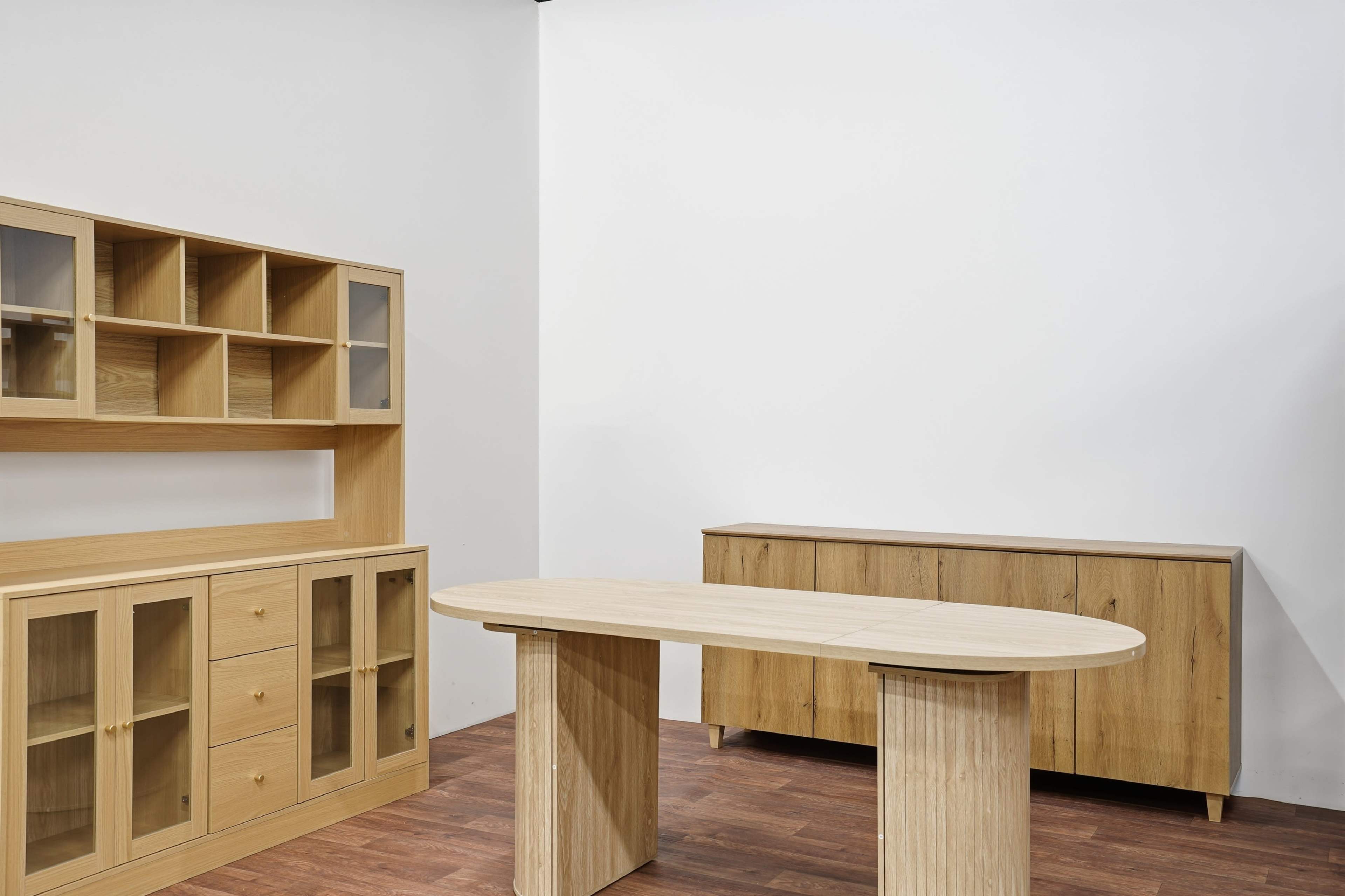 The image shows a minimalistic interior with a wooden oval table in the center, flanked by two wooden storage units against the walls.