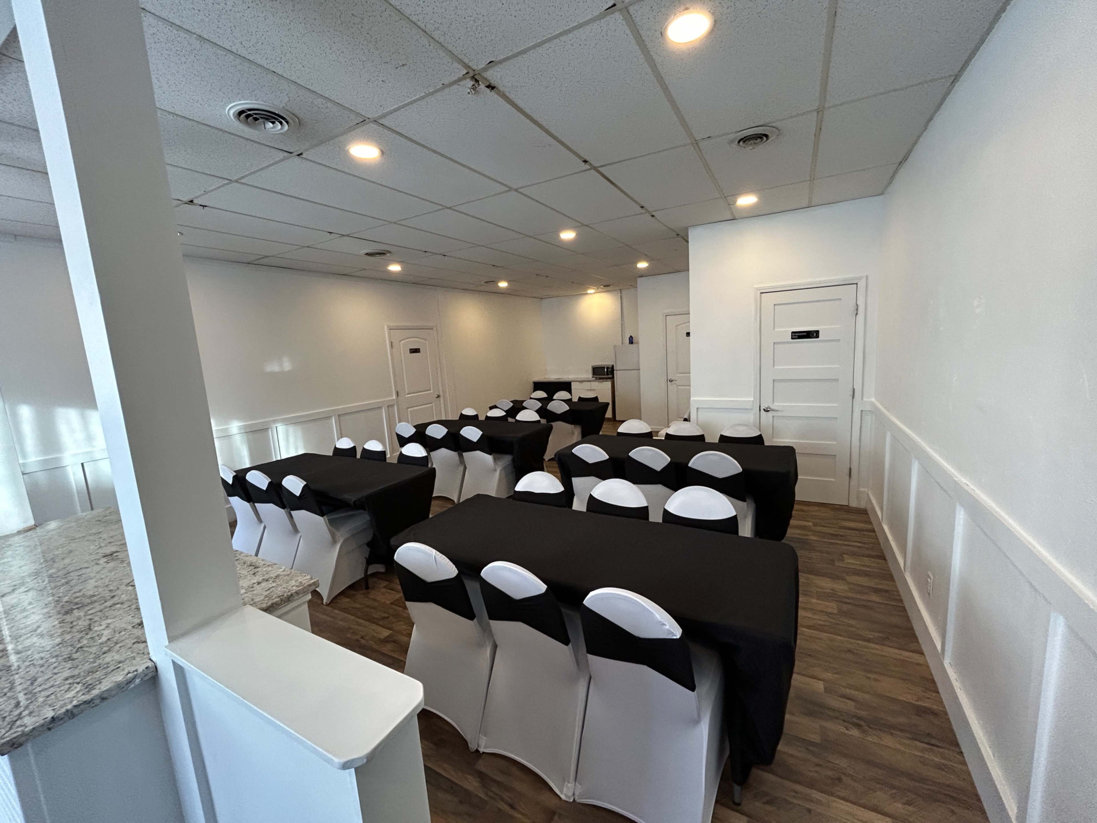 The image shows a spacious meeting room set with multiple tables covered in black linens and arranged in rows, with white chairs at each table.