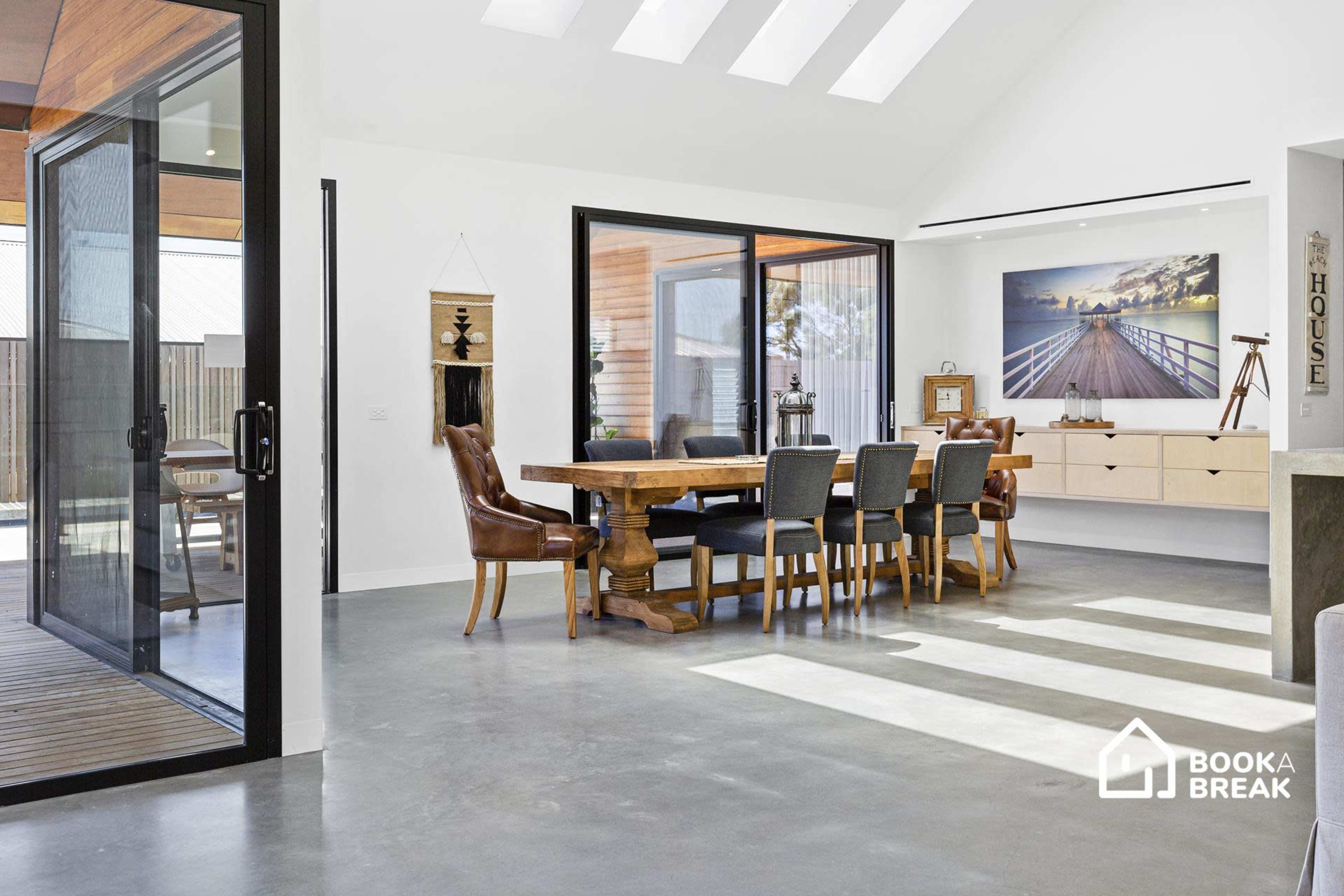 A modern dining area featuring a large wooden table surrounded by upholstered chairs, with large sliding glass doors leading to an outdoor space.