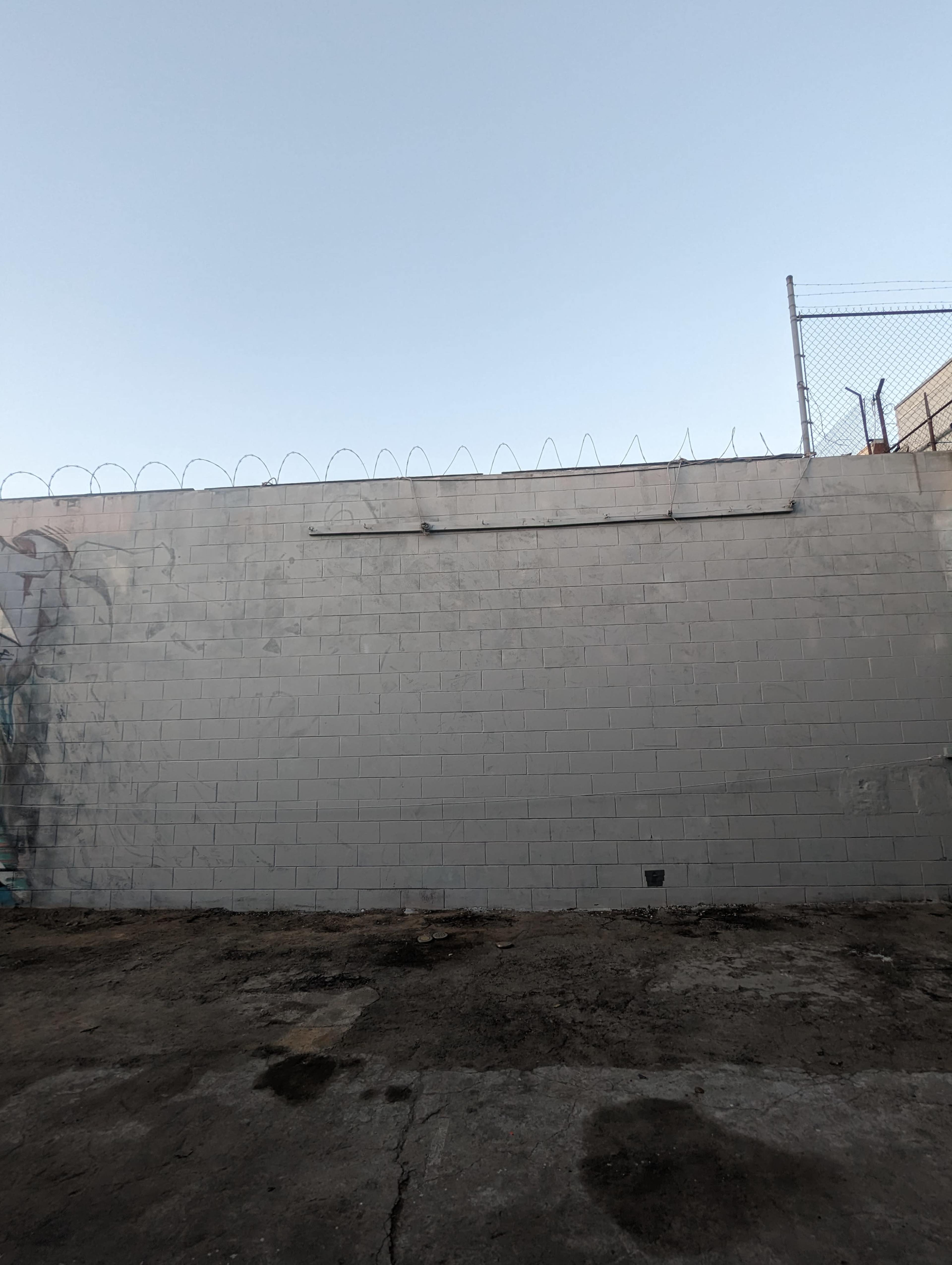 A concrete wall with barbed wire at the top stands against a clear sky.
