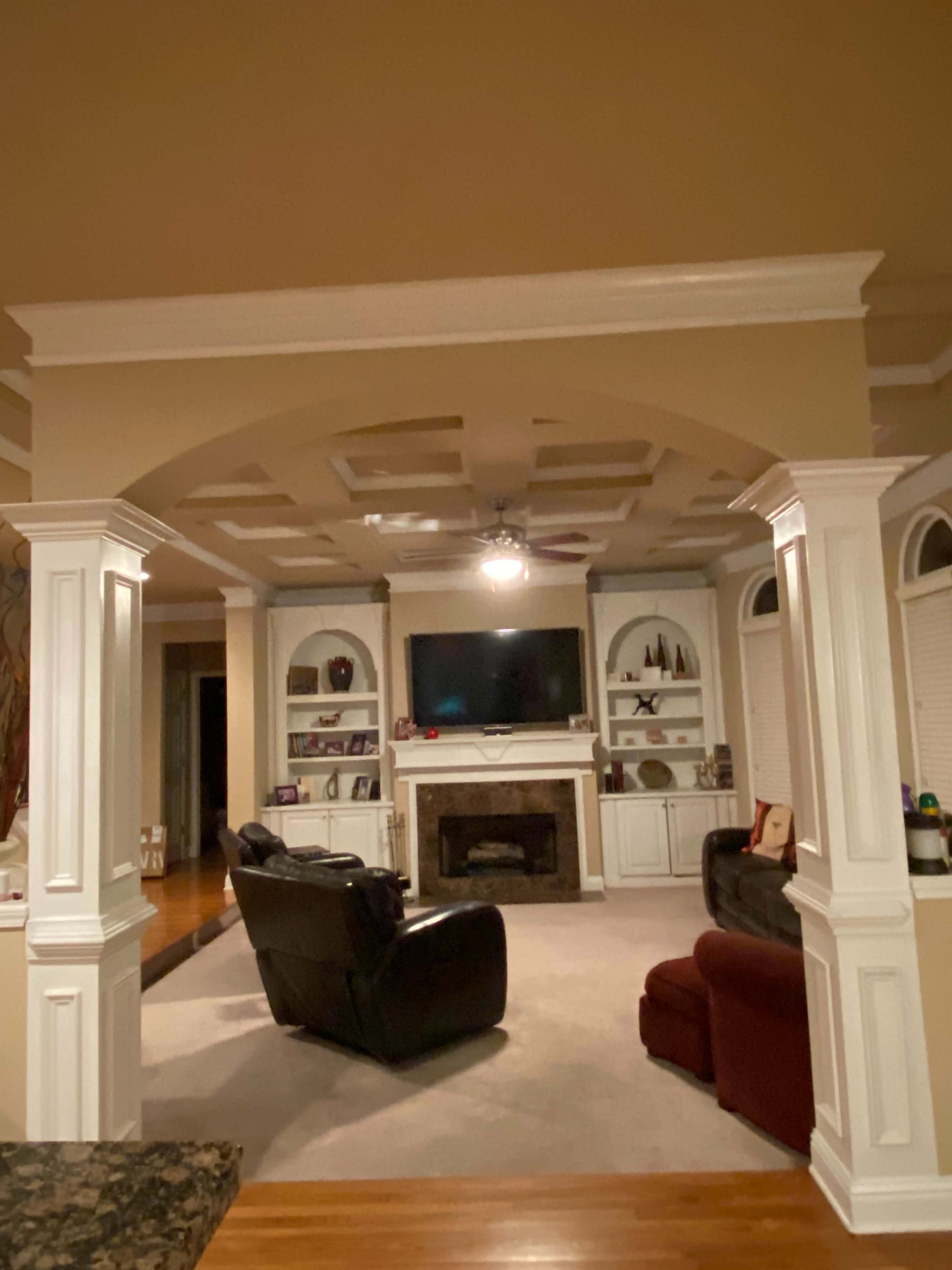 A living room with a TV mounted above a fireplace, framed by white columns and featuring a black recliner and a red sofa.