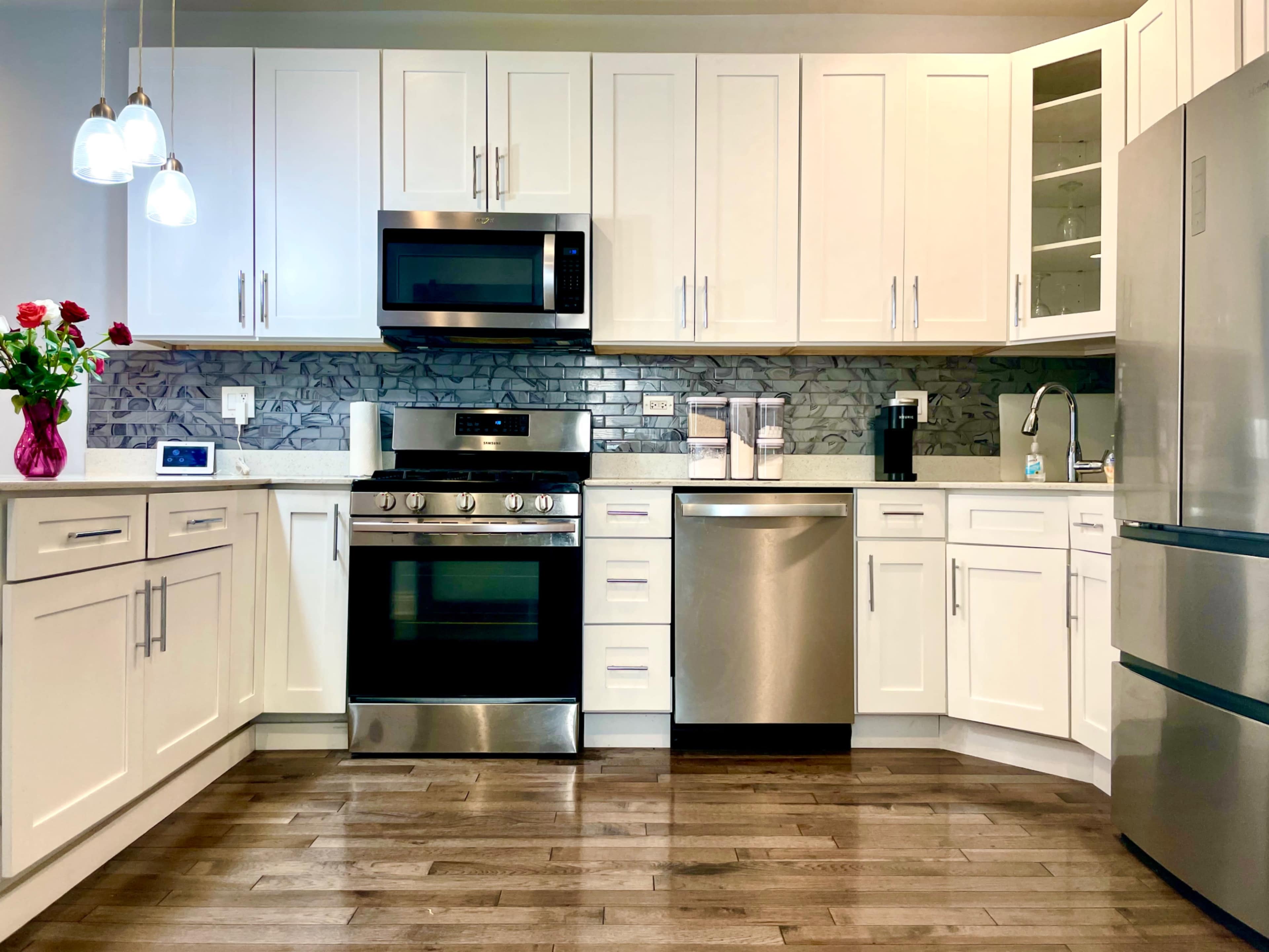 A modern kitchen with stainless steel appliances, glossy white cabinets, and a wooden floor.