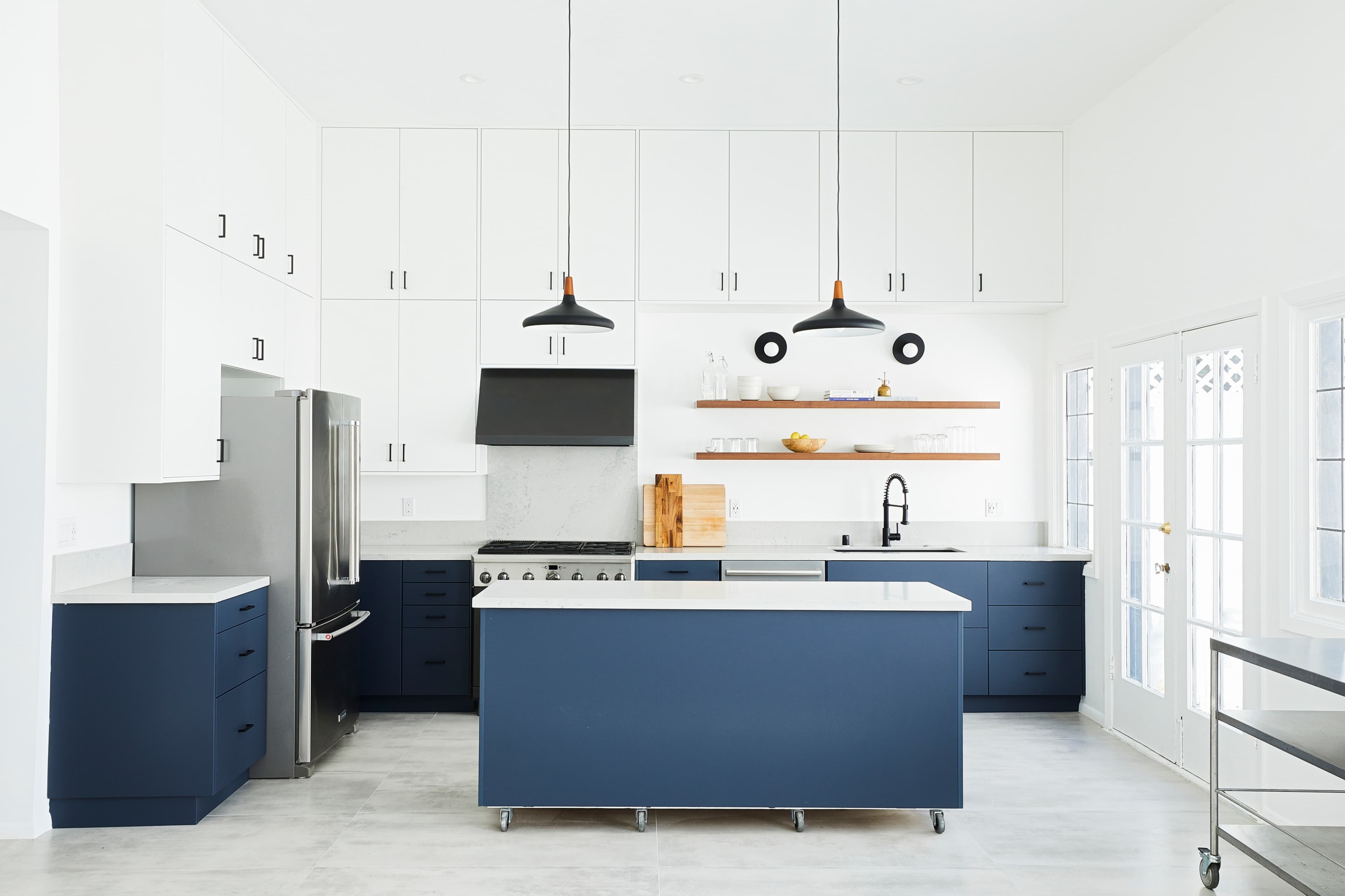 A modern kitchen with white upper cabinets, navy blue lower cabinets, a large island, and stainless steel appliances.