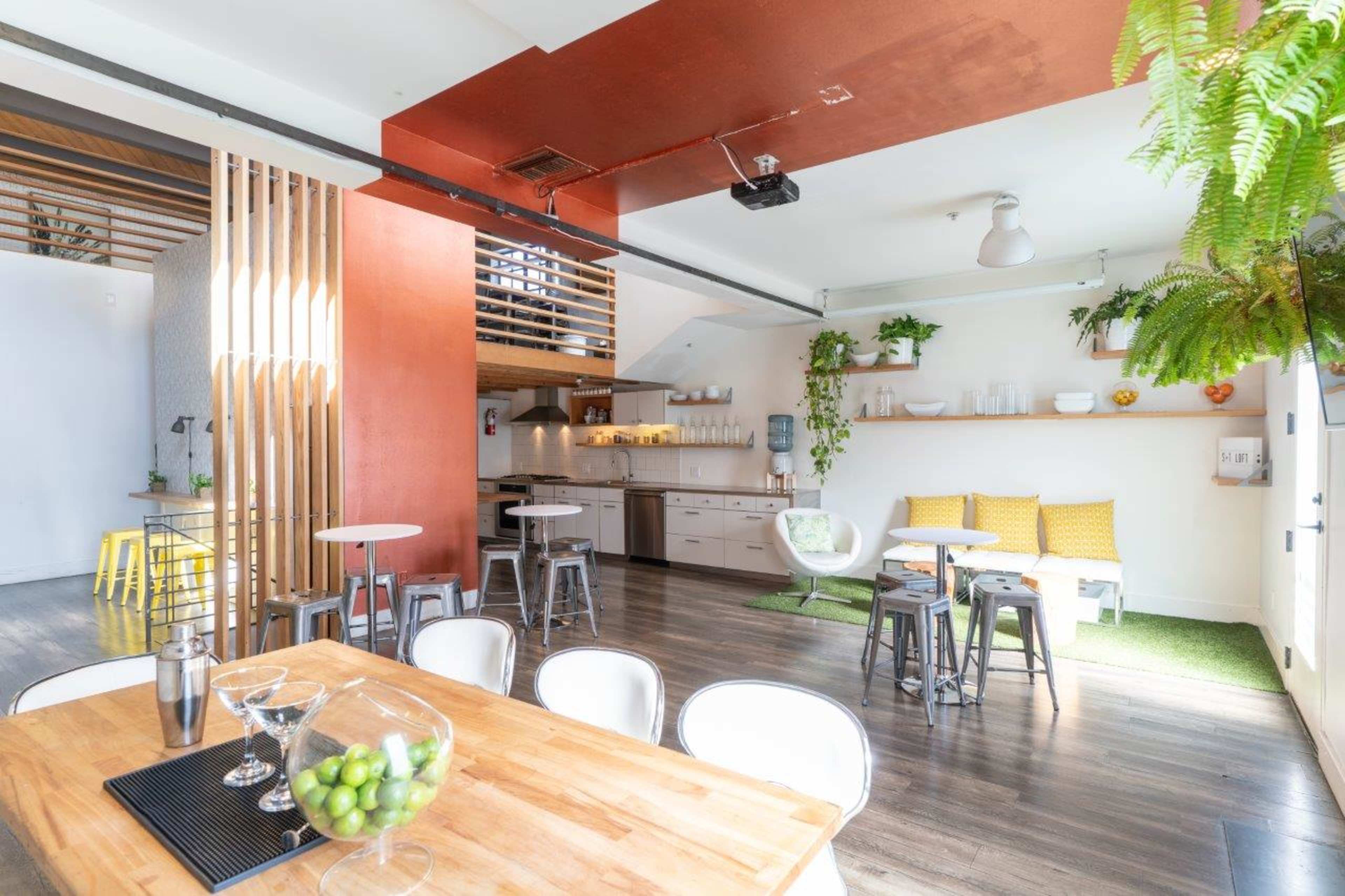 A modern kitchen and dining area with wooden and metal furniture, featuring a bar with a shaker, and green plants adding decoration.