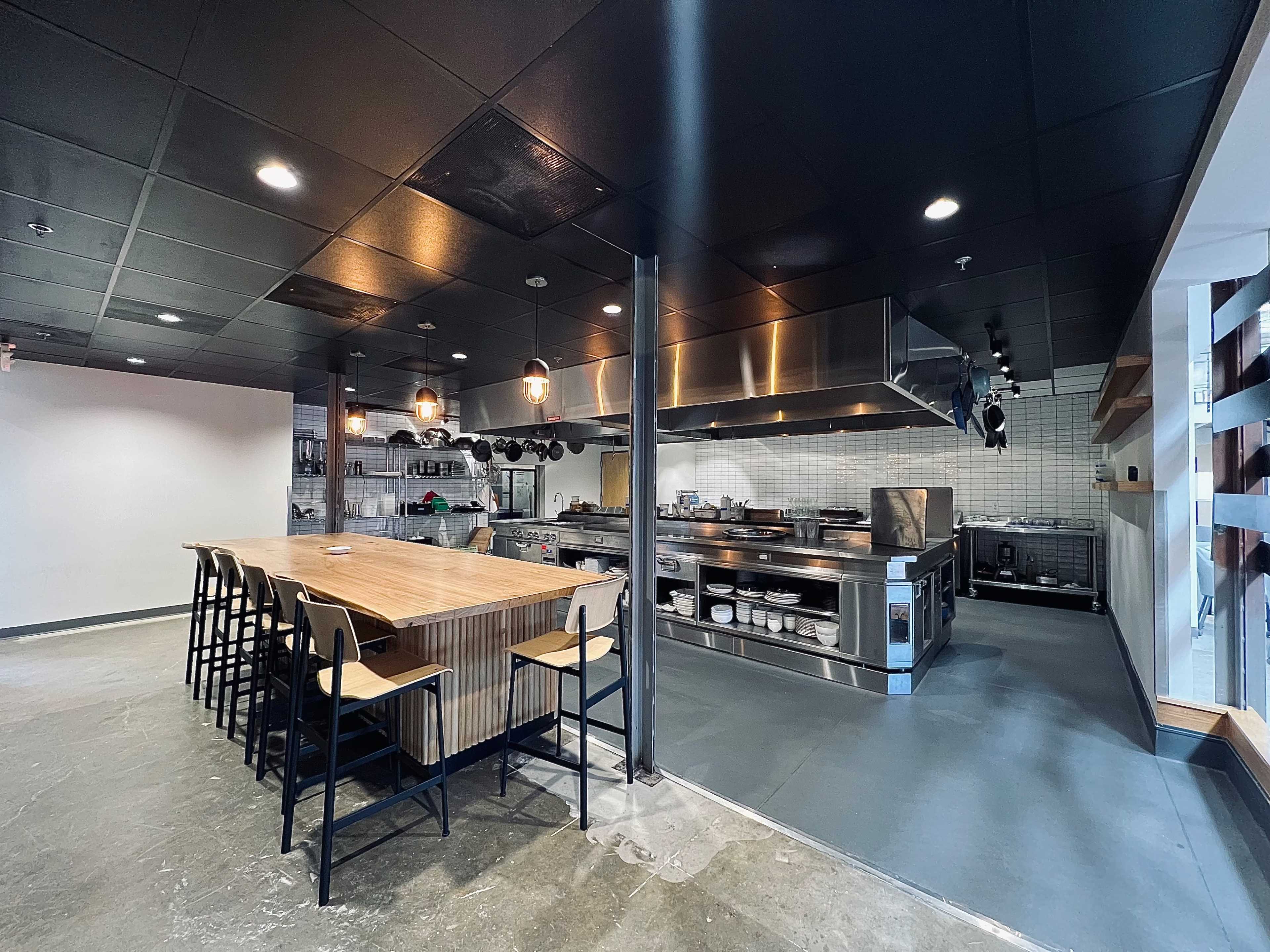 An industrial-style kitchen featuring a large wooden table and various stainless steel appliances.