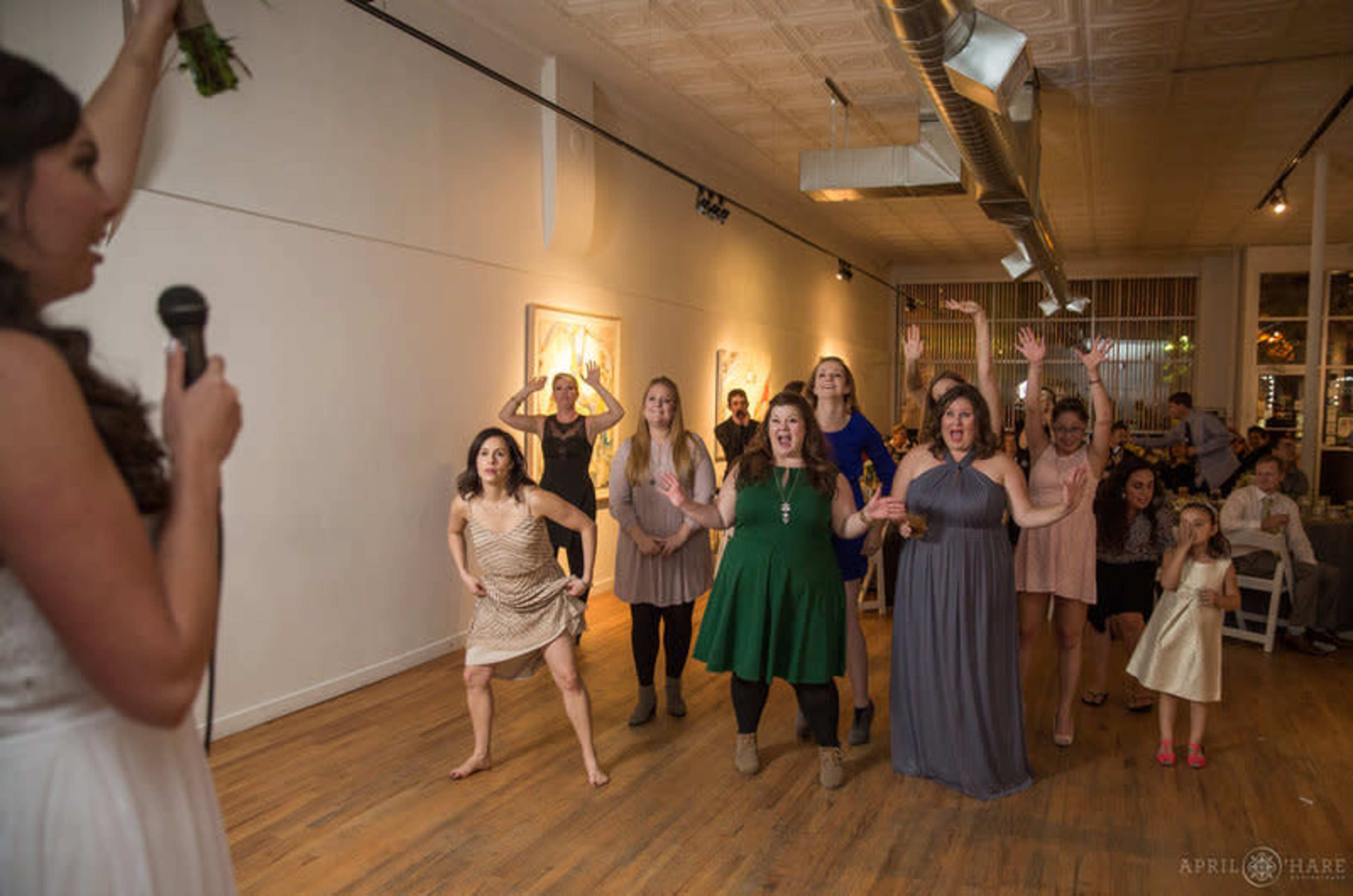 A group of women in various dresses is dancing and cheering at an indoor event.