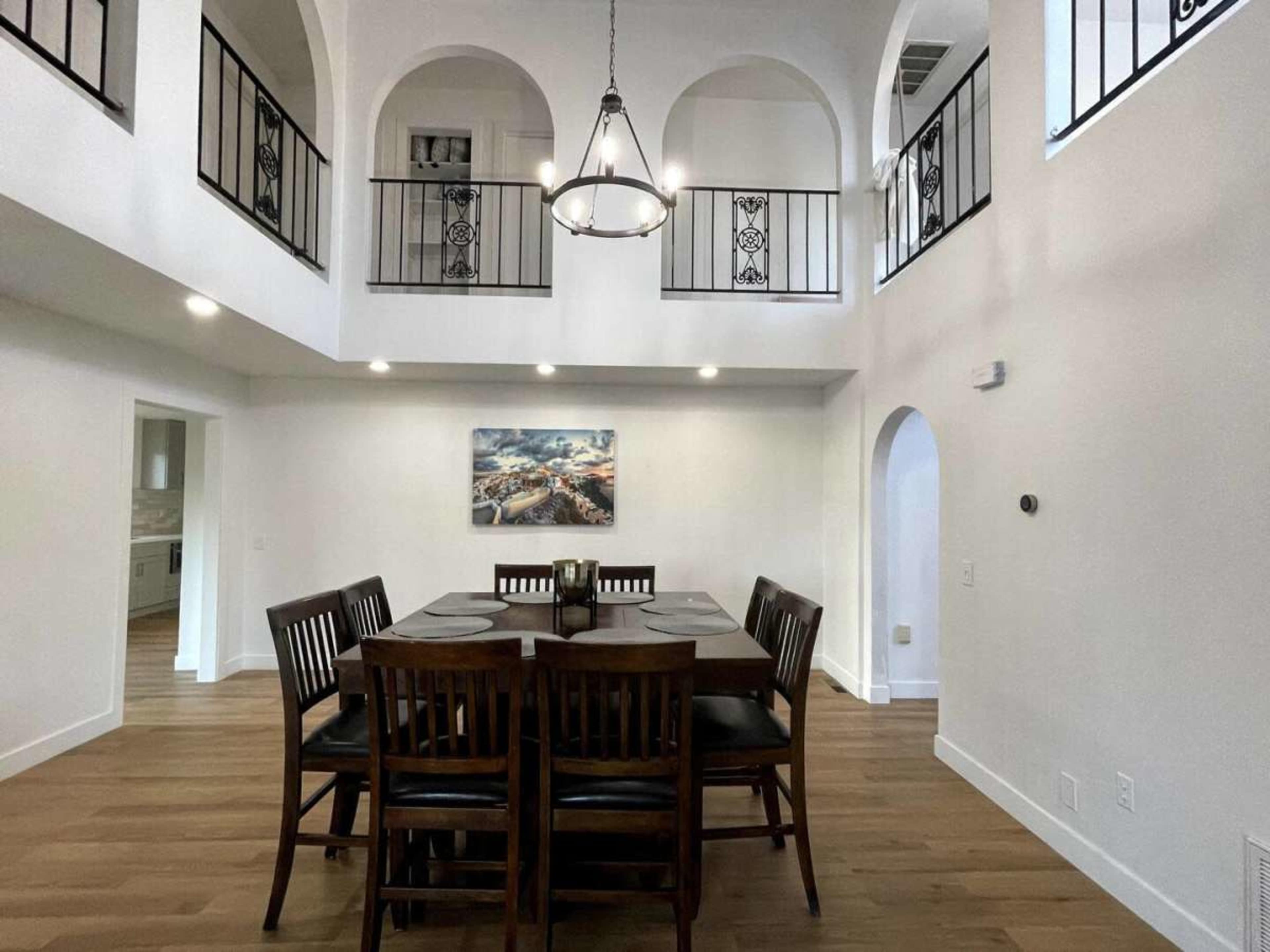 A spacious dining area features a wooden table surrounded by chairs, with arched ceilings and a chandelier above.