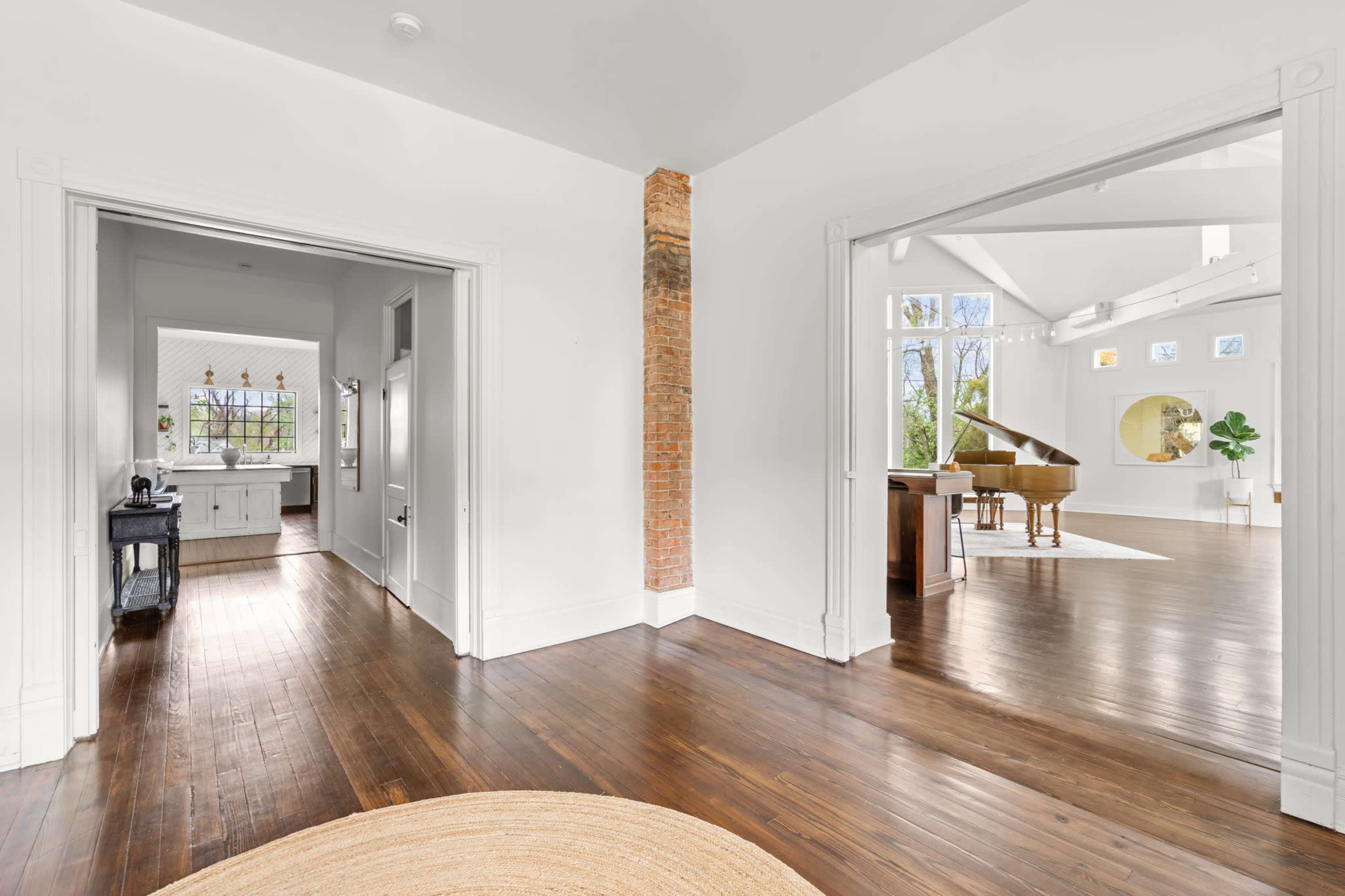 A spacious, well-lit interior features an open layout connecting a living area with a grand piano and a kitchen in the background.