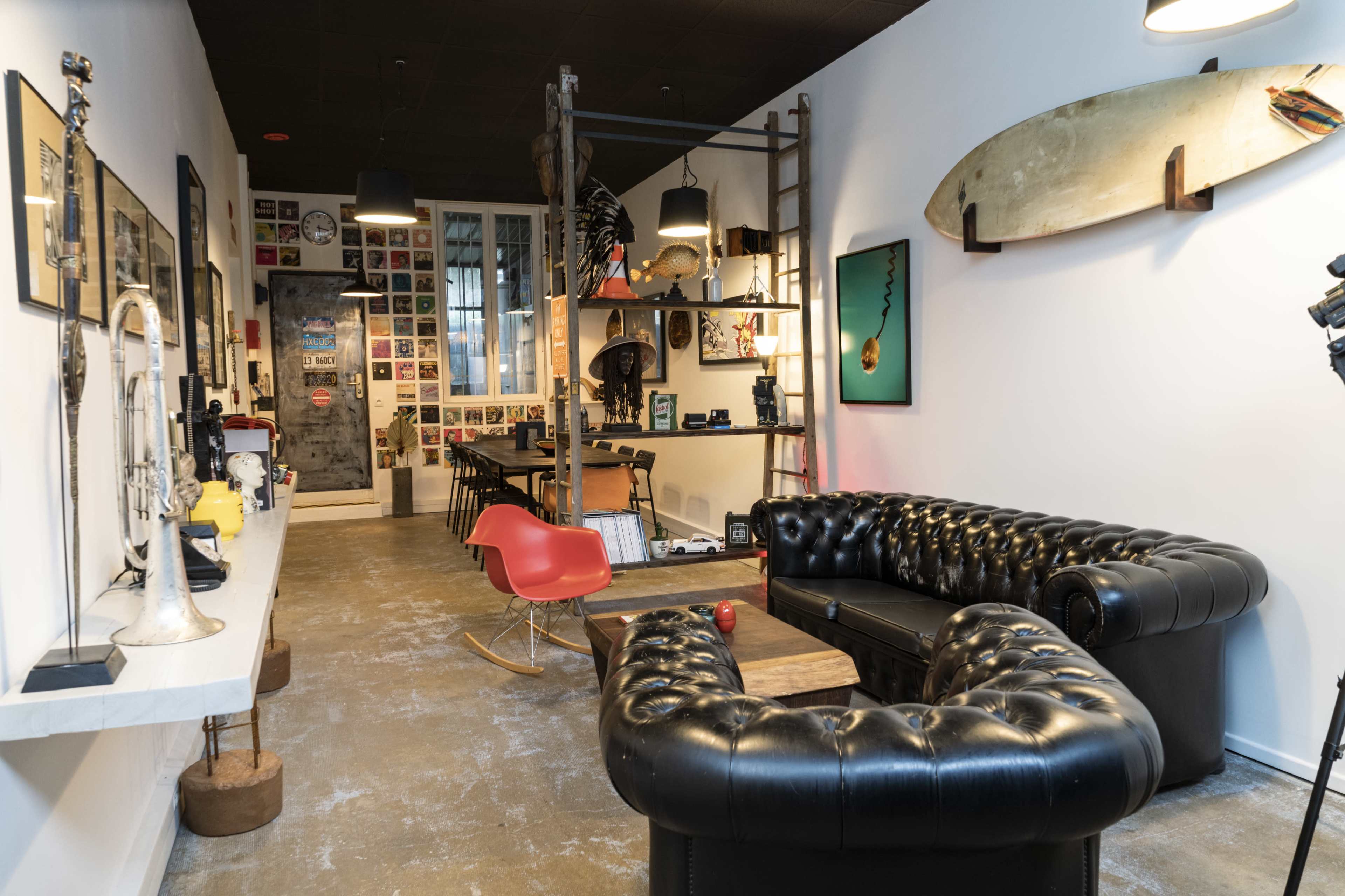 A modern interior features a black leather chesterfield sofa, a wooden table, and wall art in an open space with industrial decor elements.