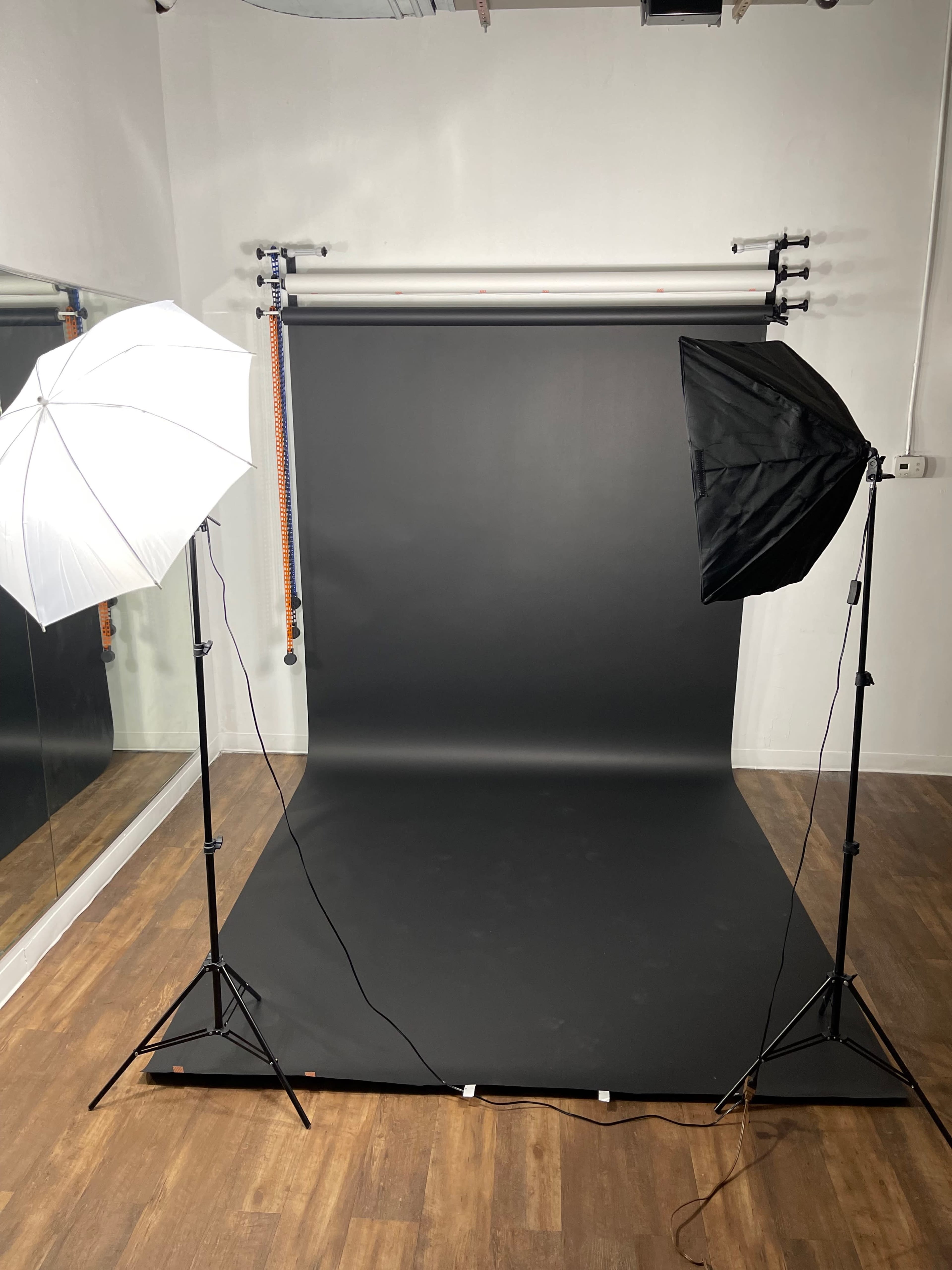 A photography studio with a black backdrop and two lighting setups positioned on either side.