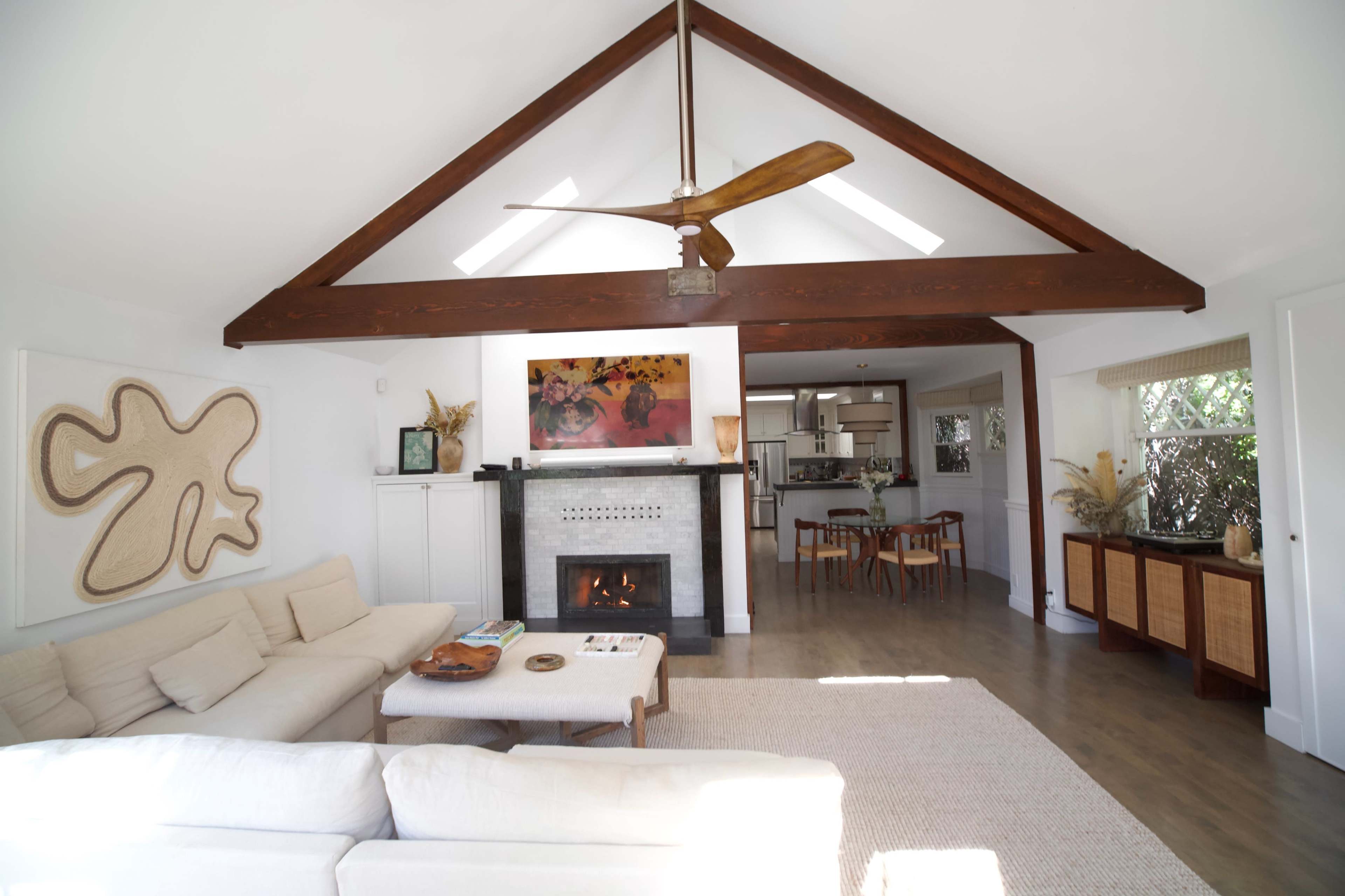 A spacious living room features a high ceiling with exposed wooden beams, a fireplace, and a comfortable seating area with a coffee table and decor.