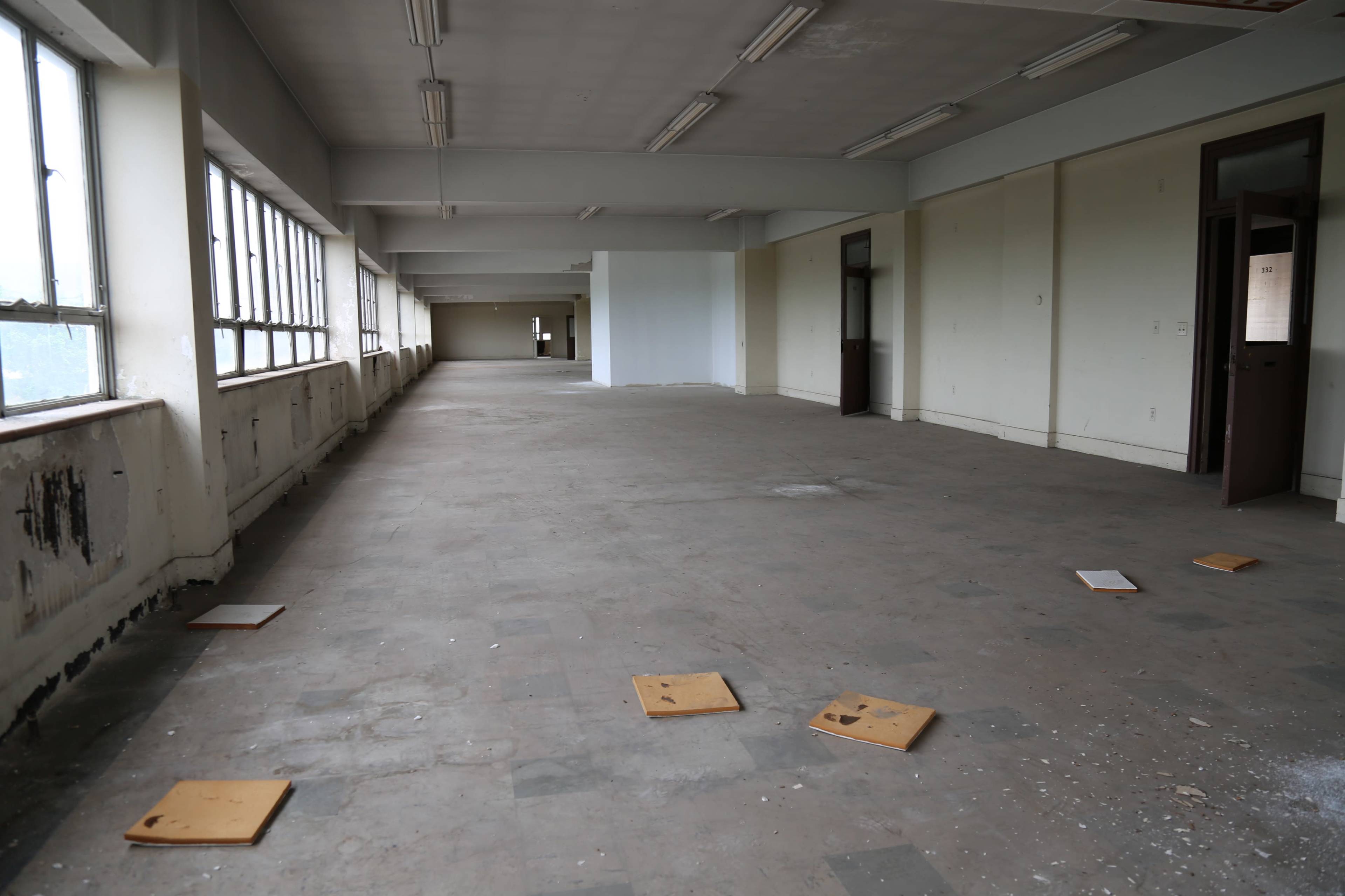 An empty, dimly lit room with a bare, dusty floor and several wooden boards scattered across it.