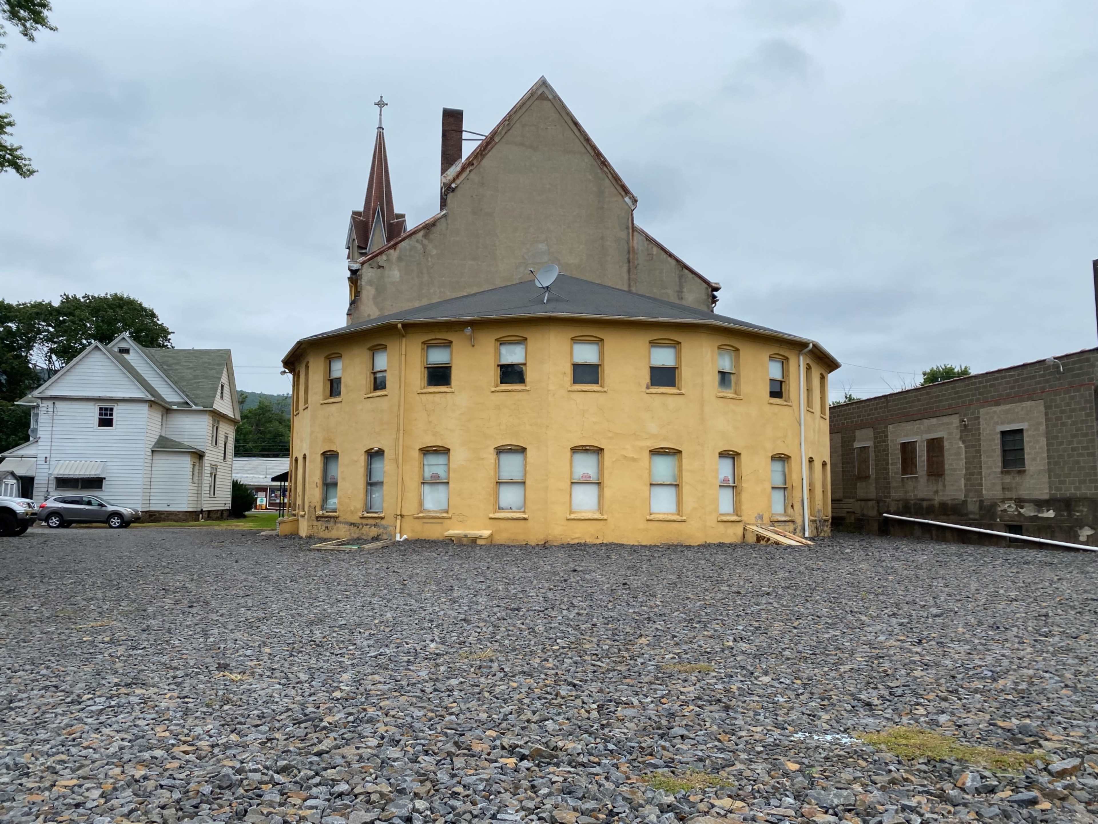 A circular, yellow building with multiple windows and a steeple in the background, set against a rocky terrain.