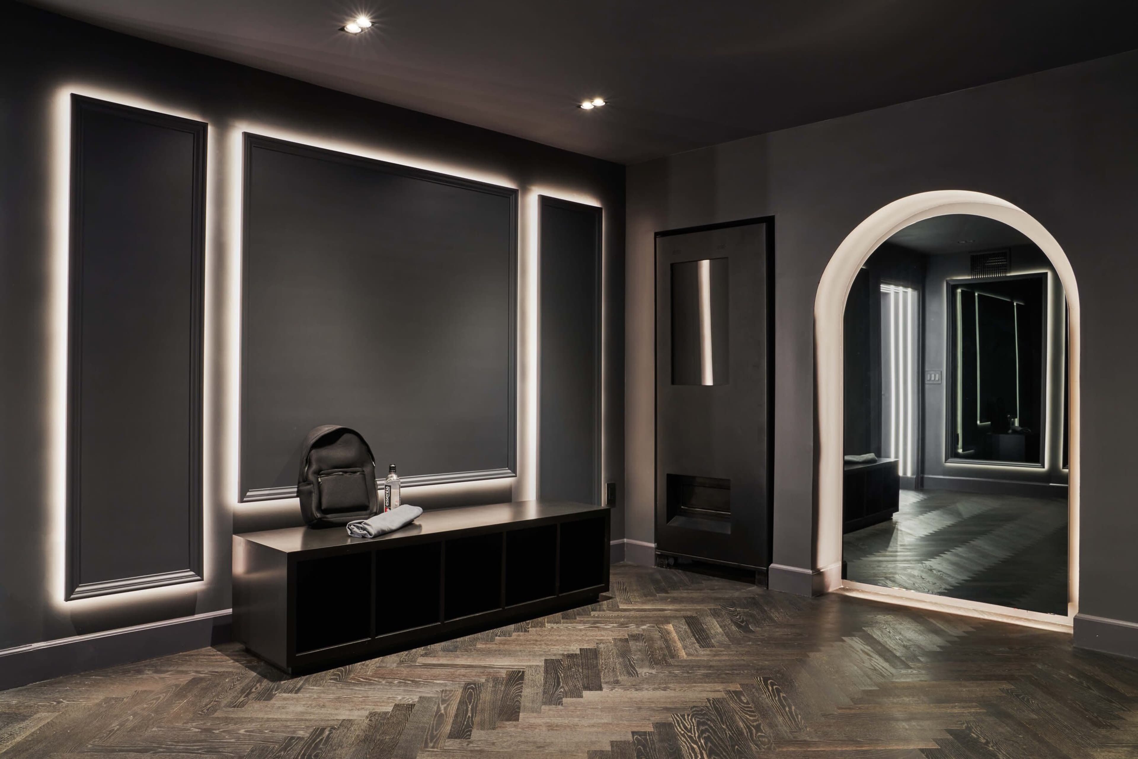 The image shows a modern interior space with dark walls, a sleek black storage unit, and an arched doorway leading to a mirrored area.