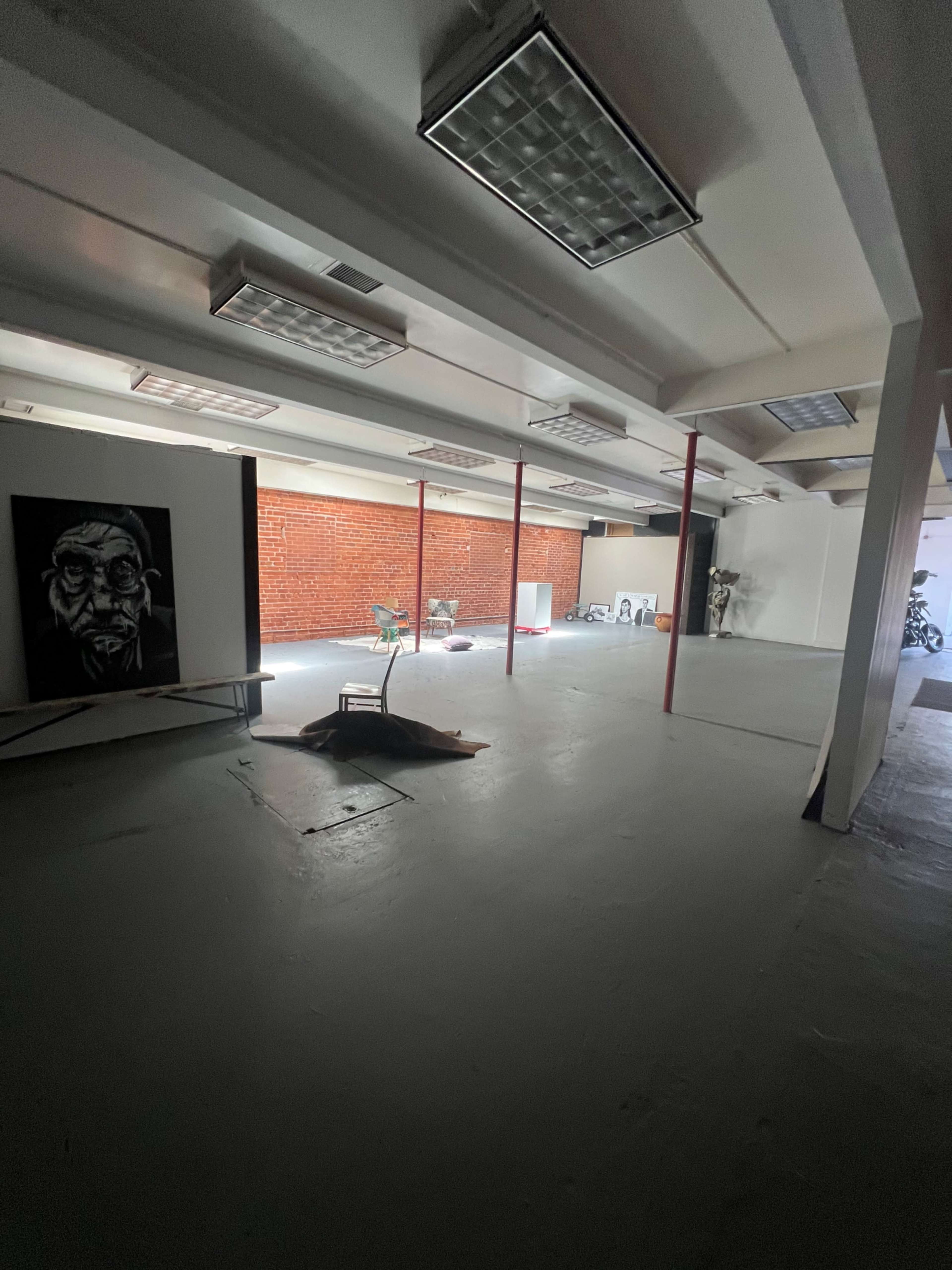 The image shows a spacious, empty room with exposed red brick walls, industrial lighting, and various furniture scattered throughout.