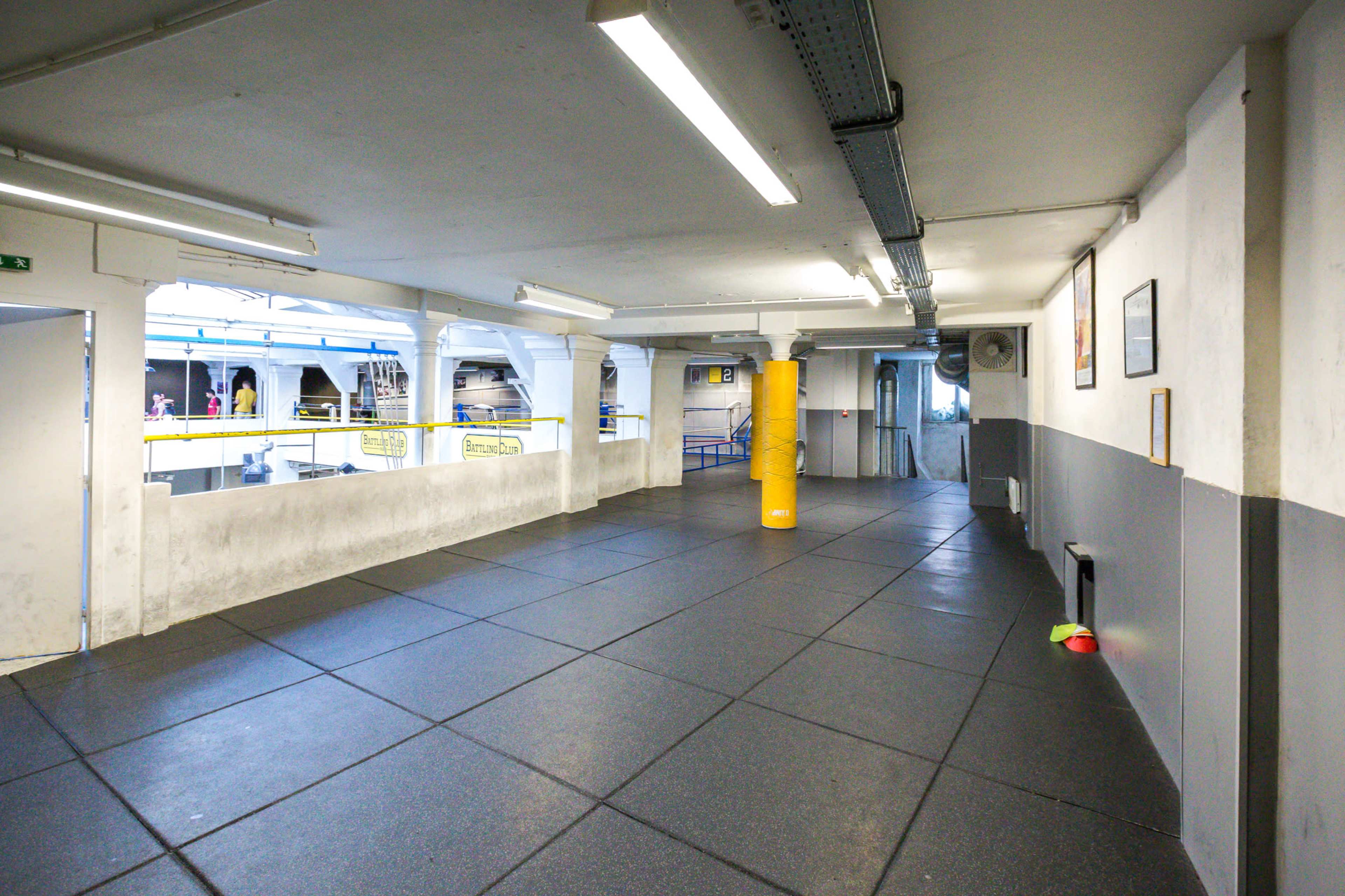 An empty training area with rubber flooring, a yellow punching bag, and a doorway leading to another space.