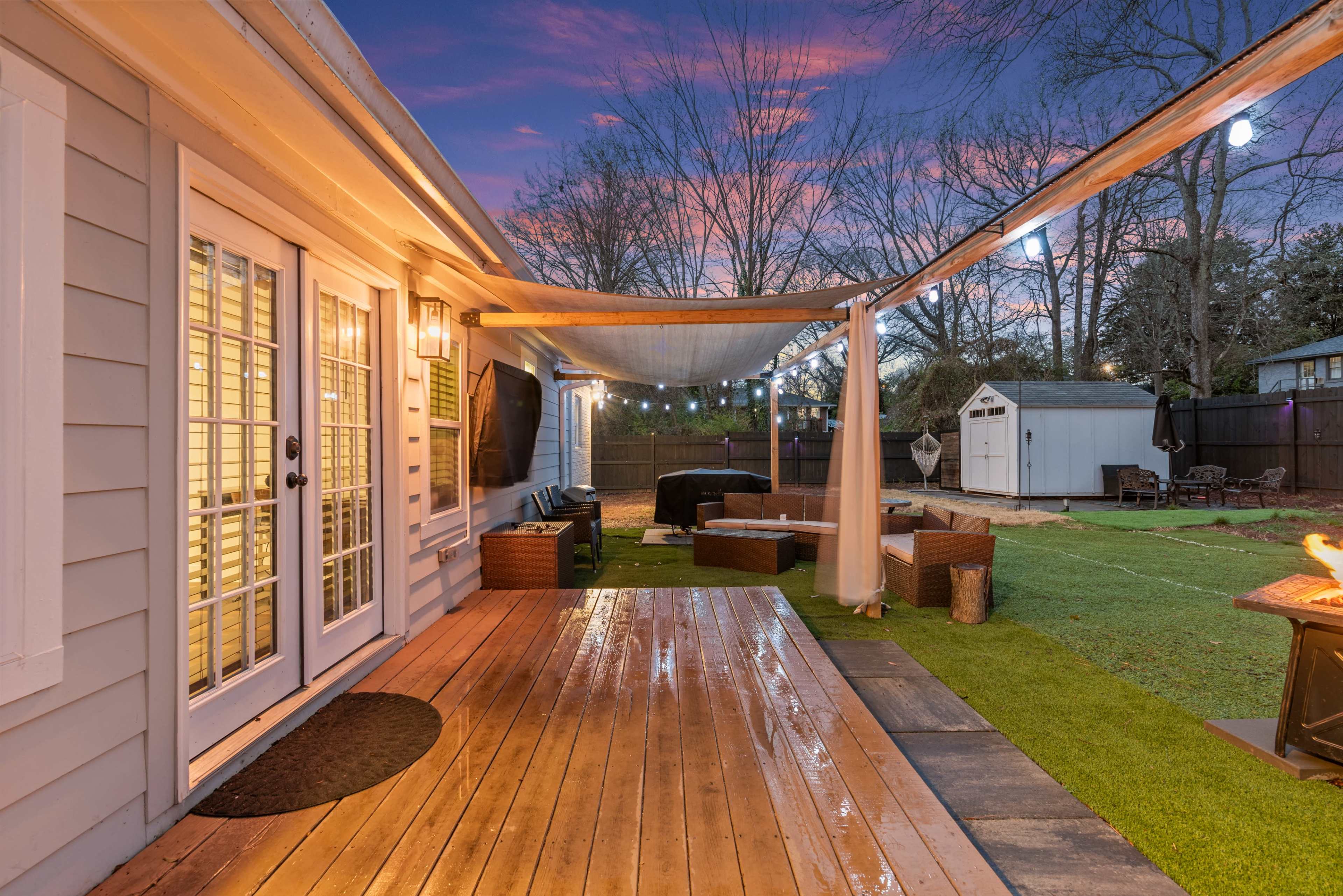 The image shows a backyard patio with a wooden deck, outdoor furniture, and a shed, set against a colorful sunset sky.