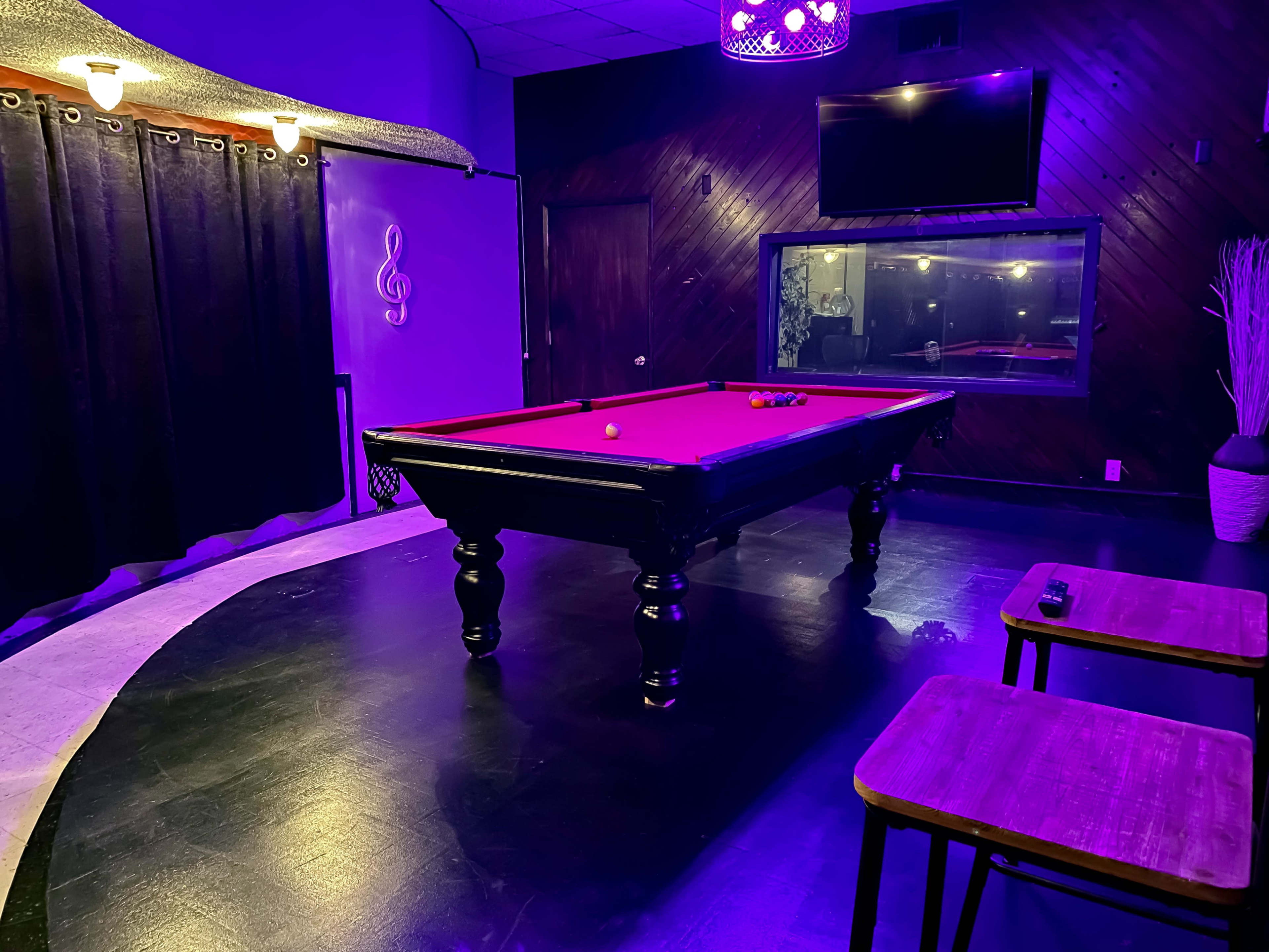 A billiards table sits in a dimly lit room adorned with purple lighting and dark wood accents.