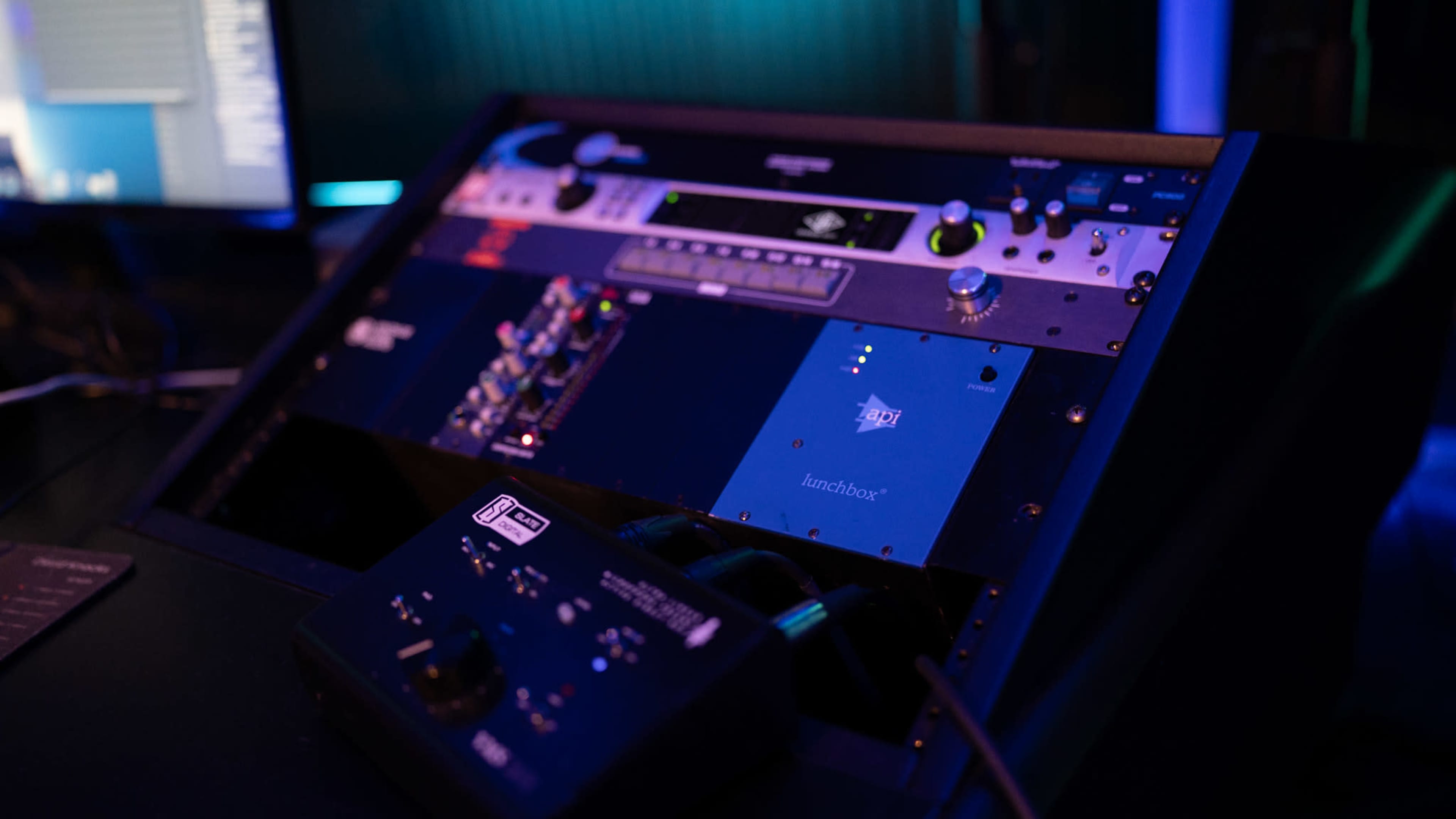 The image shows a close-up of an audio mixing console with various controls and lights illuminated.