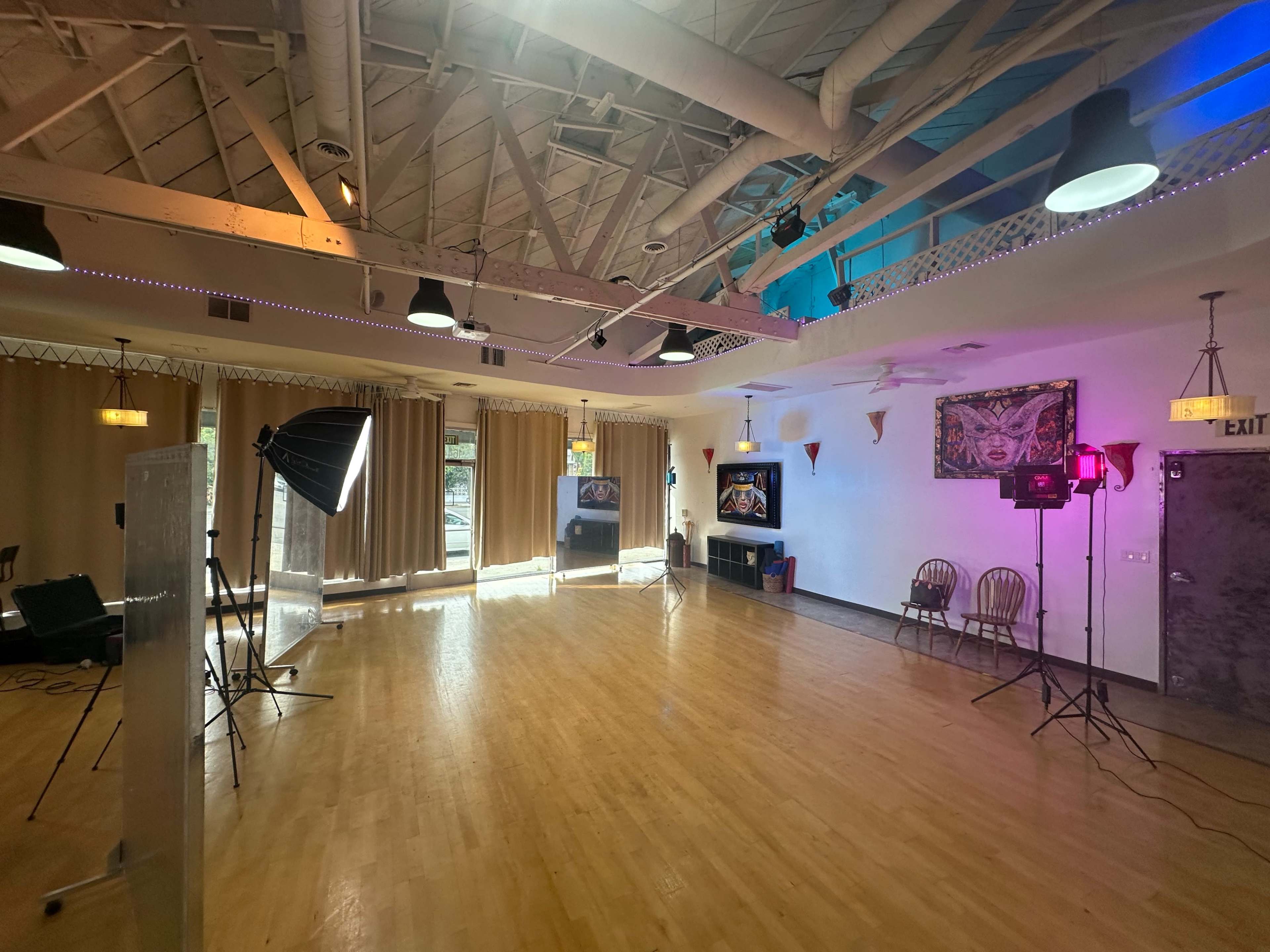 The image shows a spacious indoor studio with wooden flooring, large curtains, and various lighting equipment set up for an event or photoshoot.