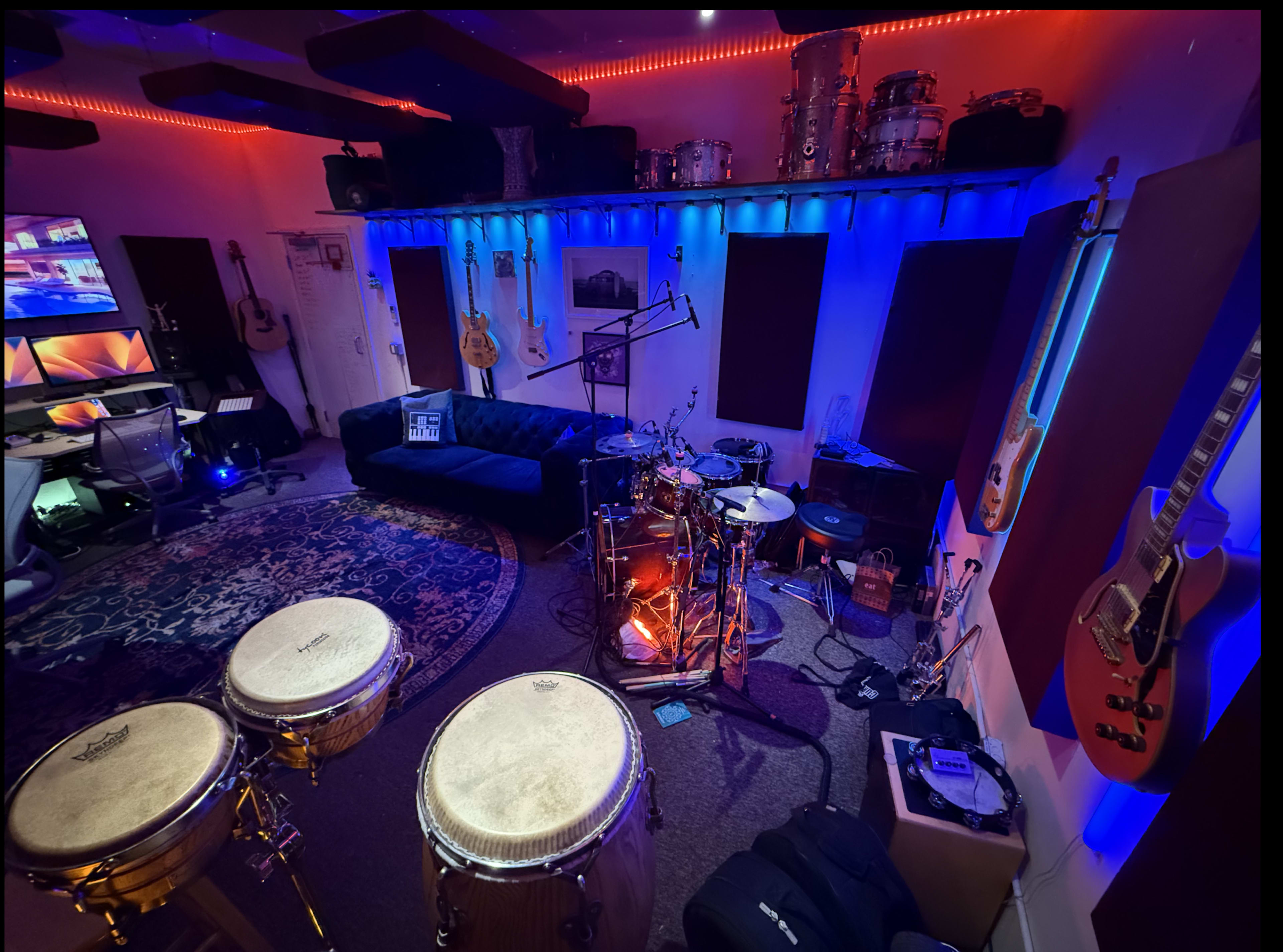 The image shows a music studio with a couch, various instruments including drums and guitars, and colorful LED lighting.