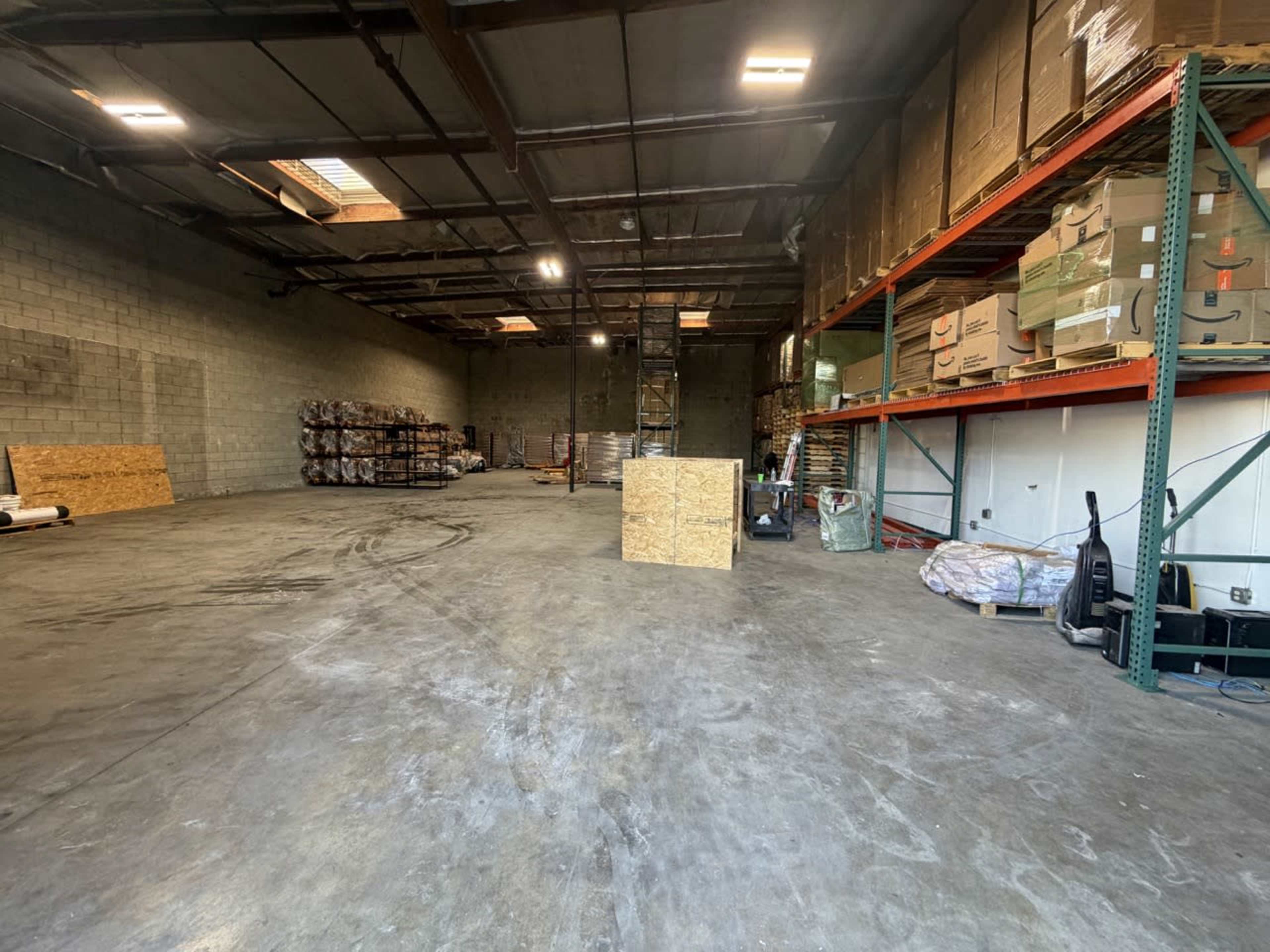 The image shows a spacious warehouse interior with stacked boxes on shelves and pallets against the walls.