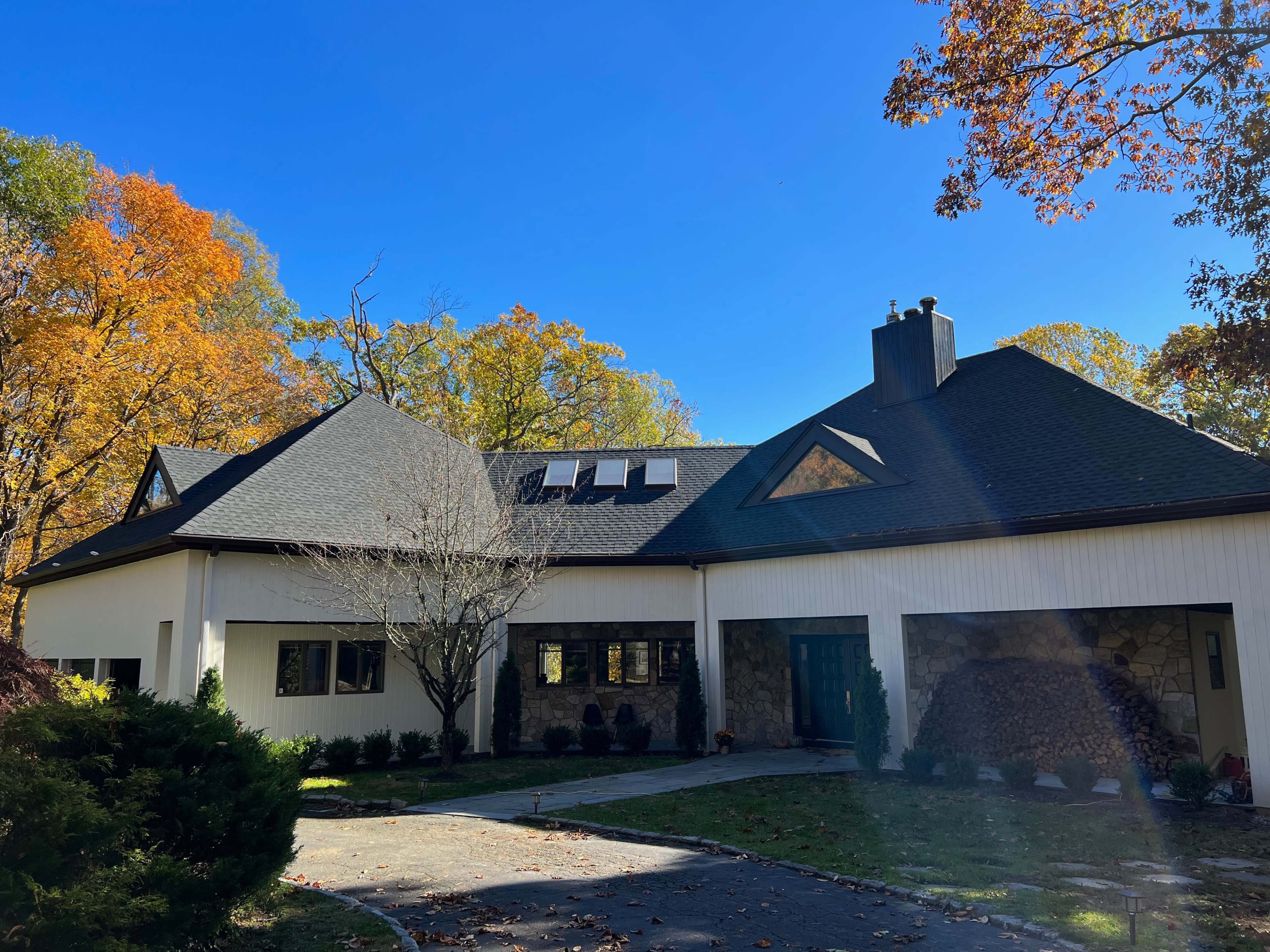 A modern house with a sloped roof and stone accents is surrounded by colorful autumn foliage.