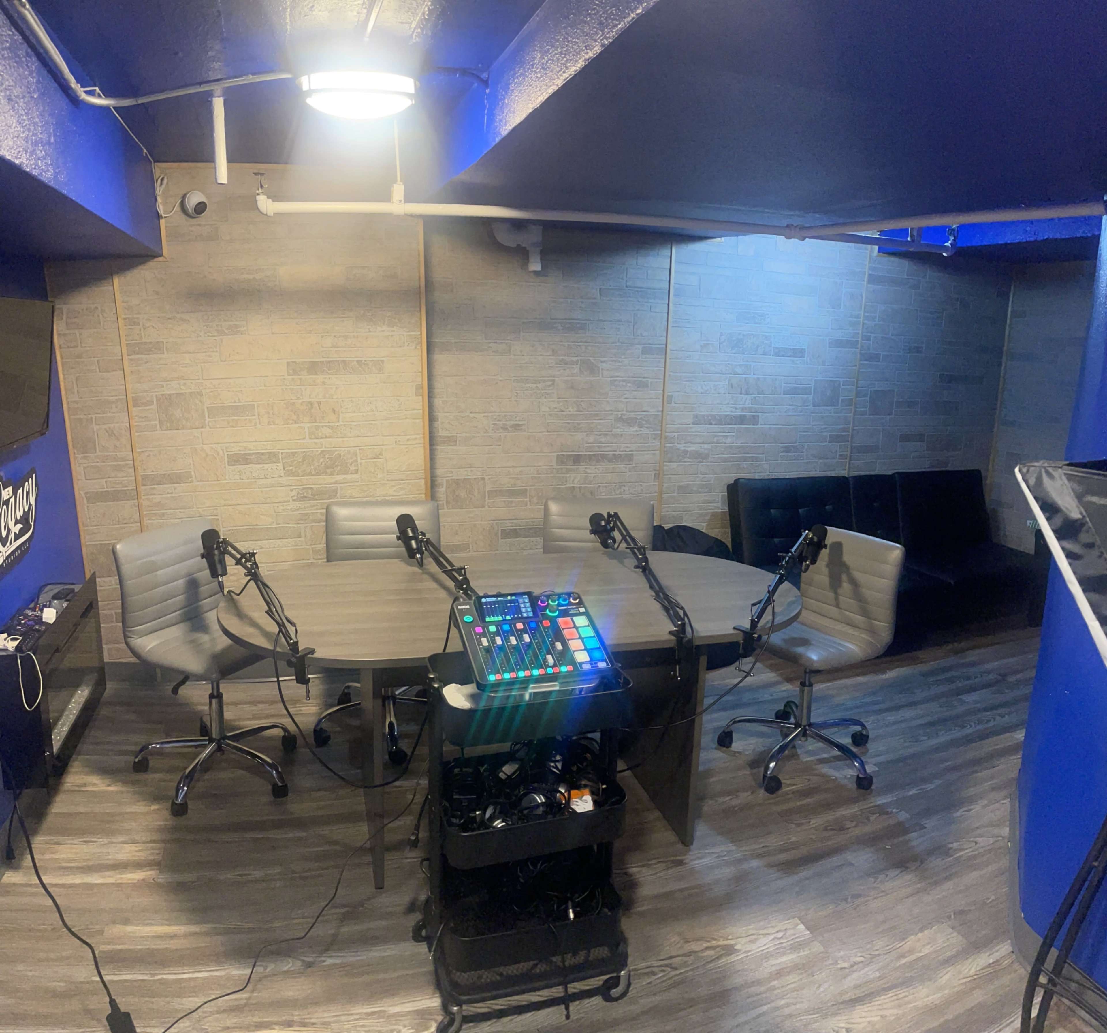 A recording studio with multiple microphones set up around a large oval table, surrounded by chairs, and a control panel on a cart.