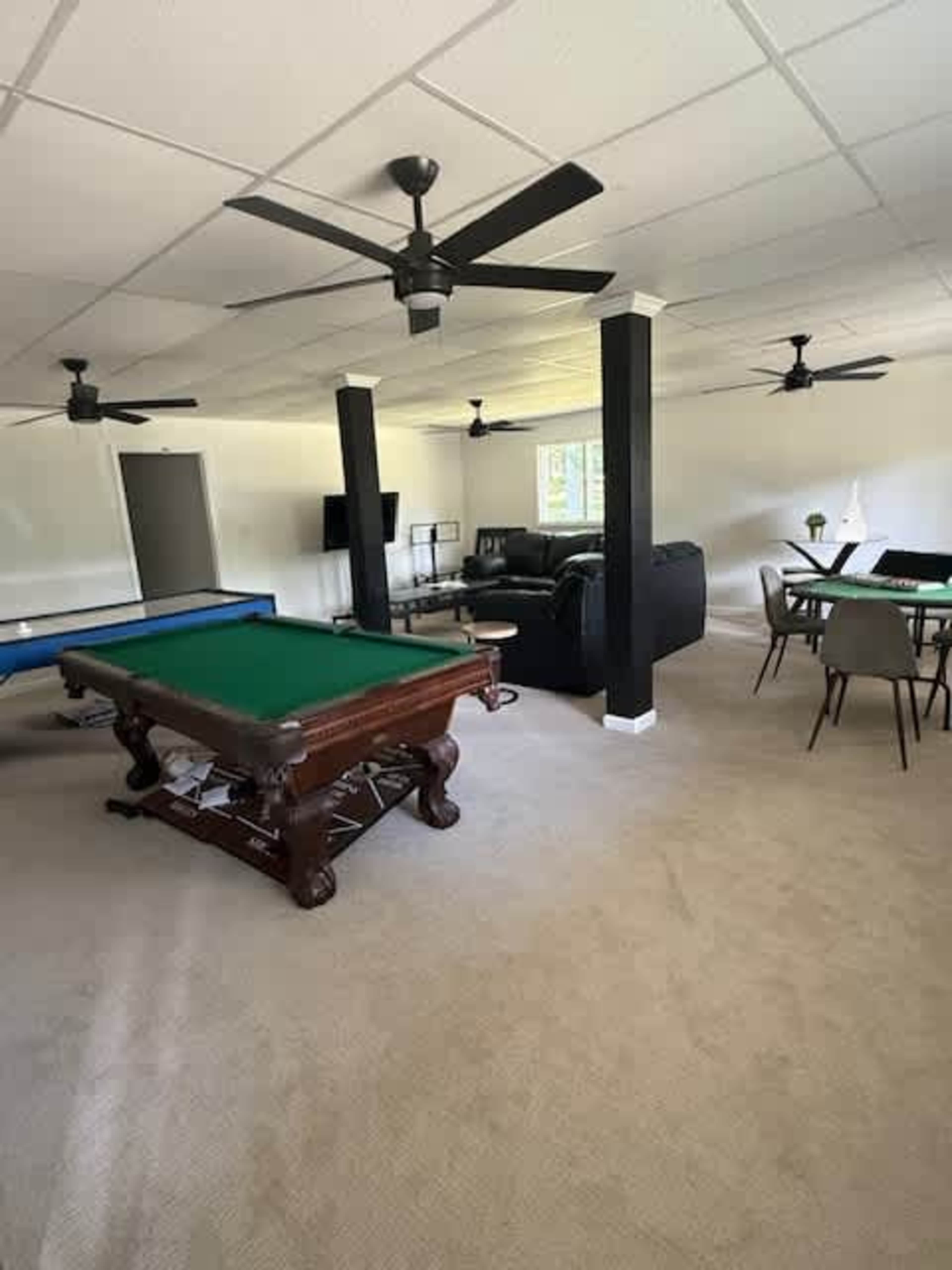 The image shows a spacious room with a pool table, a couch, a dining area, and ceiling fans.