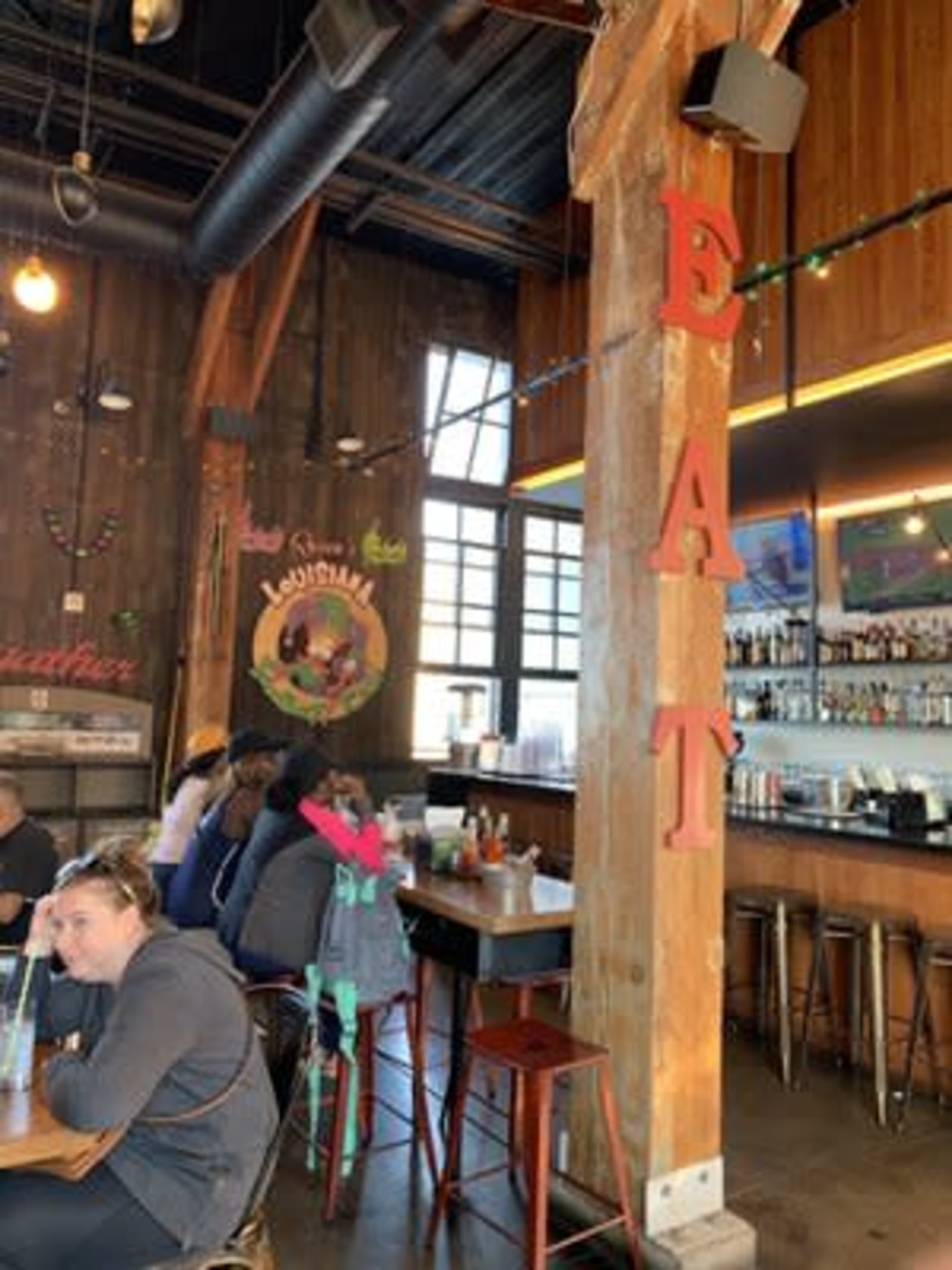 The image shows the interior of a restaurant featuring wooden beams, a bar area, and diners seated at tables.